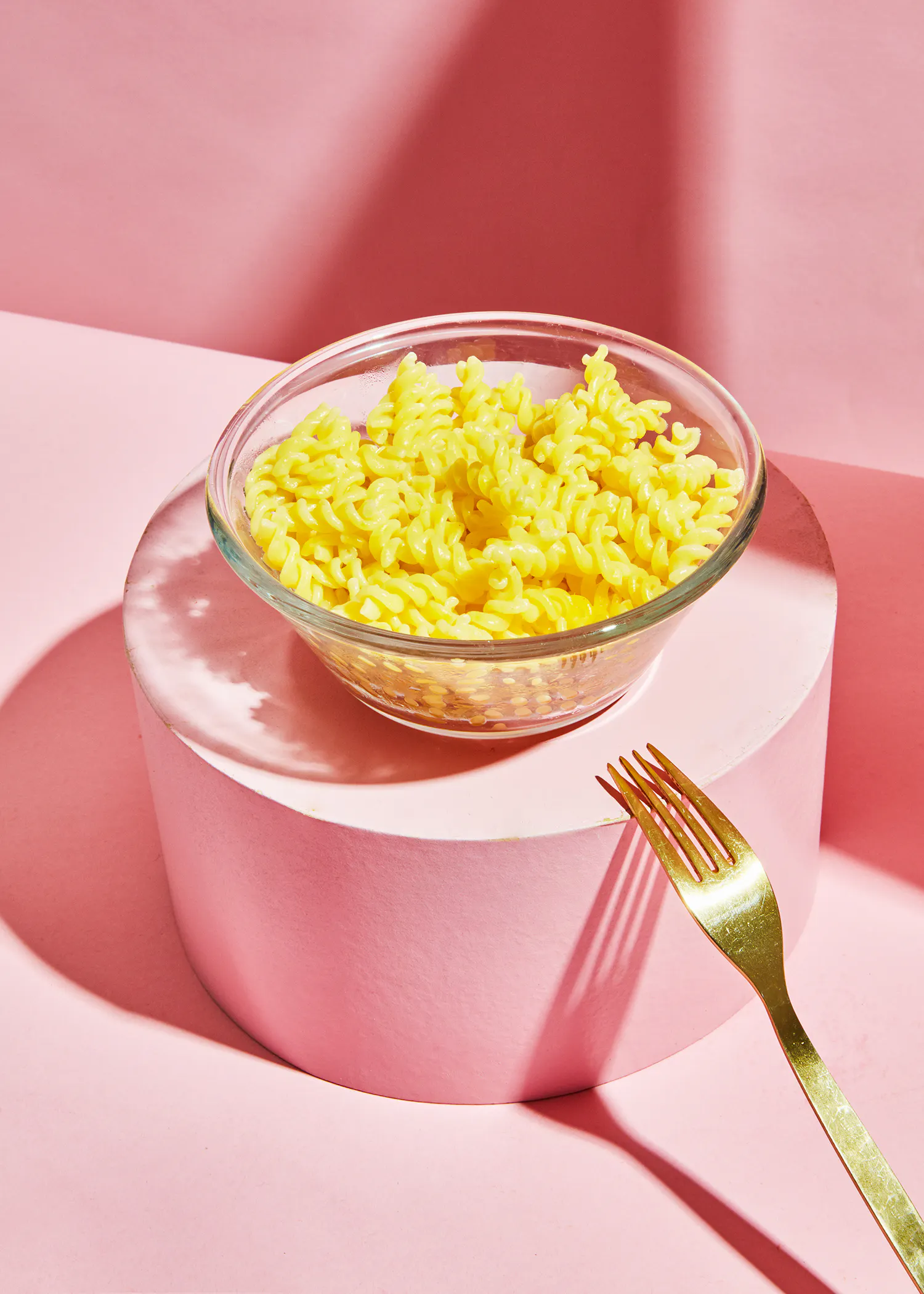 a bowl of macaroni and cheese sits on a pink block next to a fork