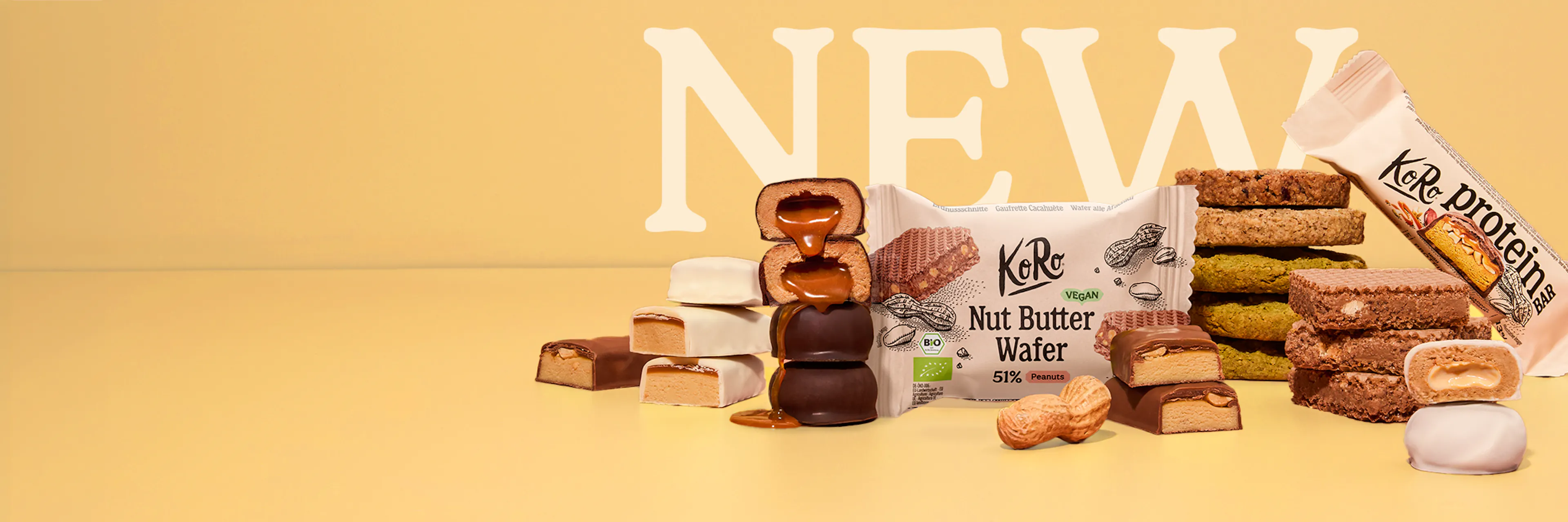 eine auswahl an koro-snacks wie nut butter wafer und proteinriegel vor einem gelben hintergrund mit dem schriftzug new.