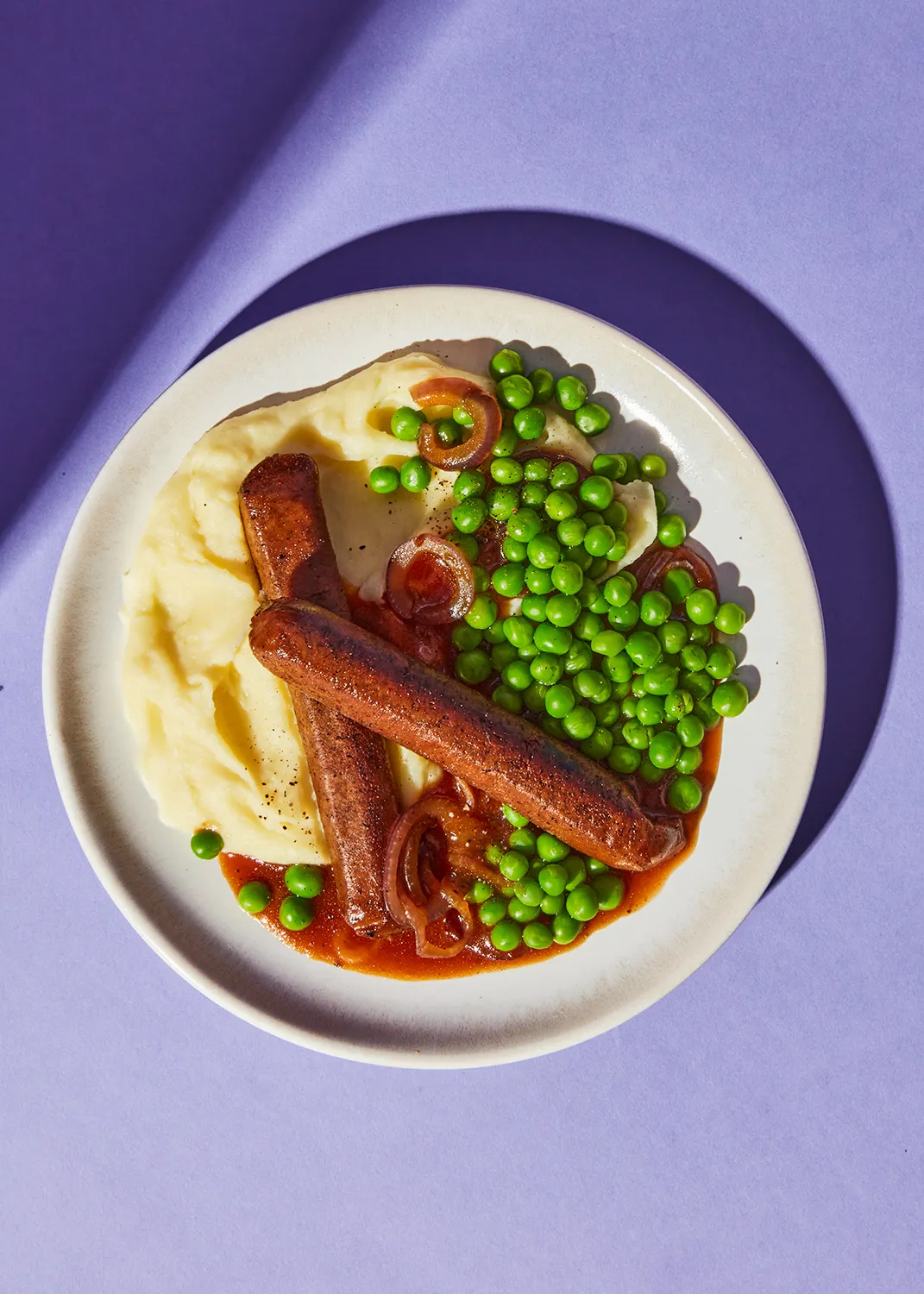 ein weißer Teller mit Kartoffelpüree und Erbsen auf einem lila Tisch