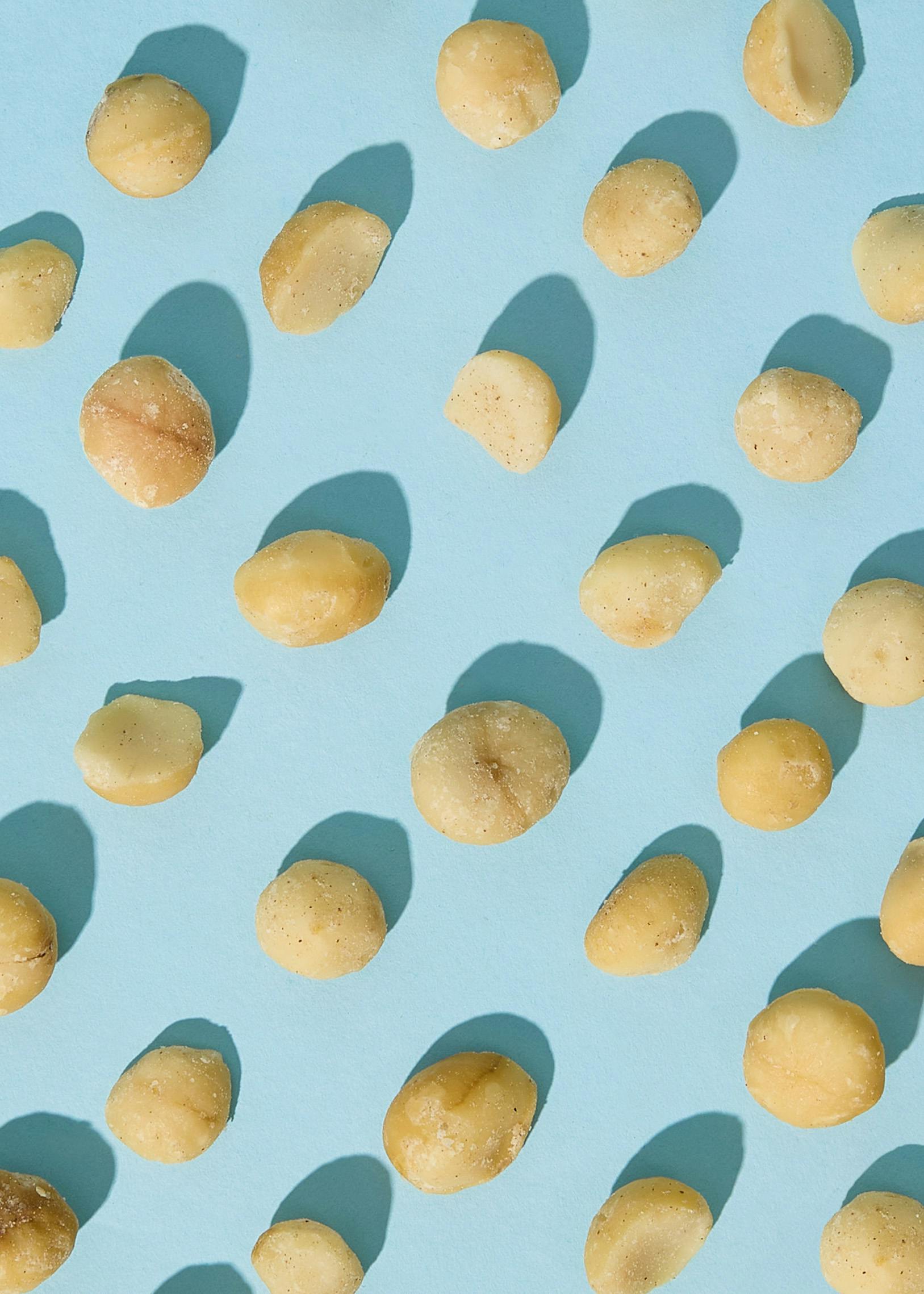 noci di macadamia chiare sparse su uno sfondo azzurro con ombre.