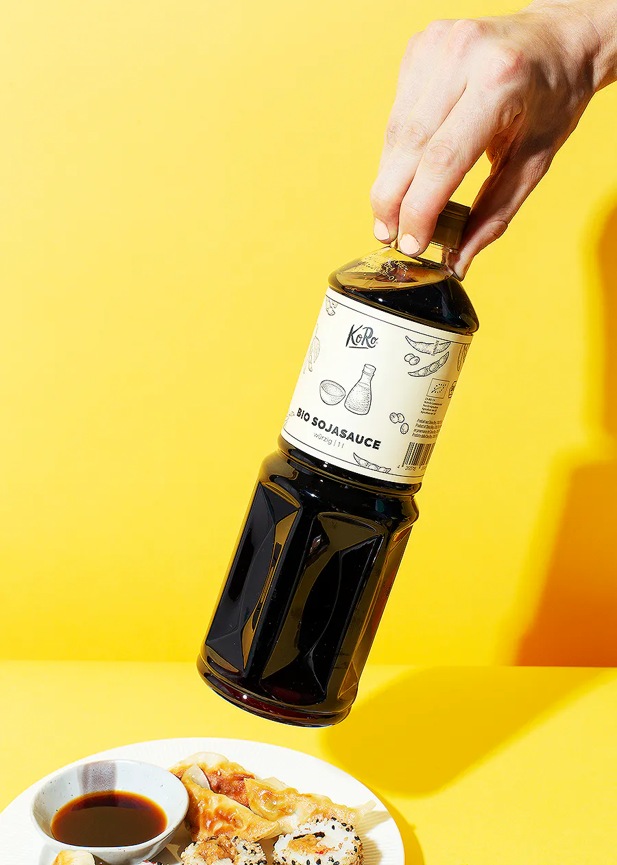 une personne verse une bouteille de sauce soja bio sur une assiette de nourriture