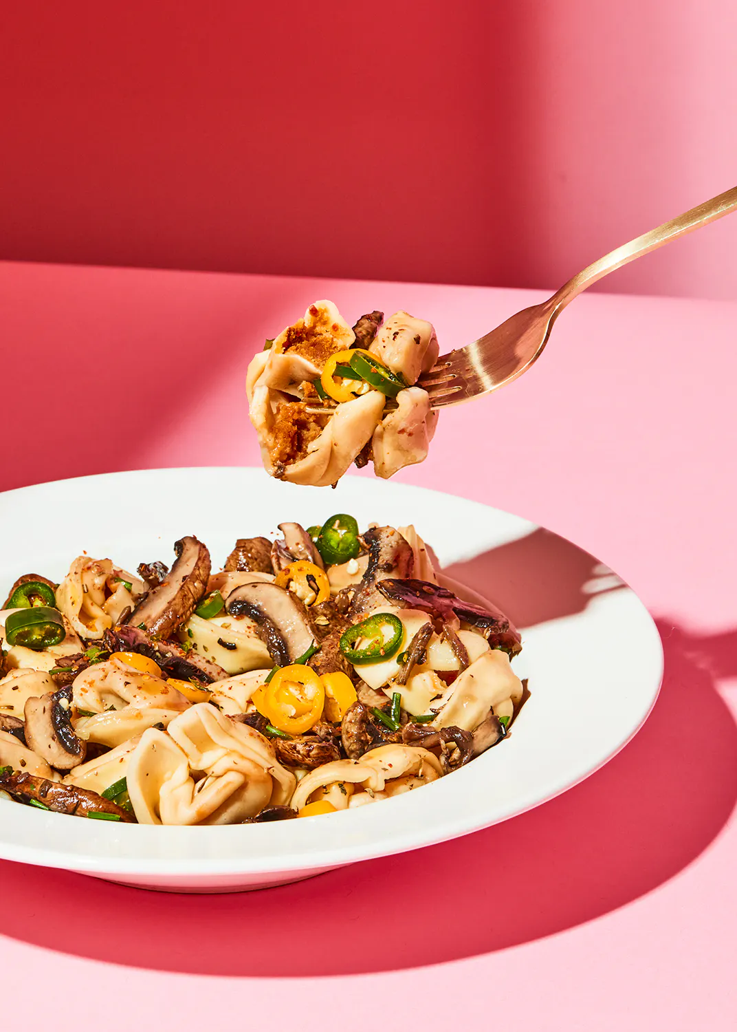 a plate of pasta with mushrooms and jalapenos on a pink background