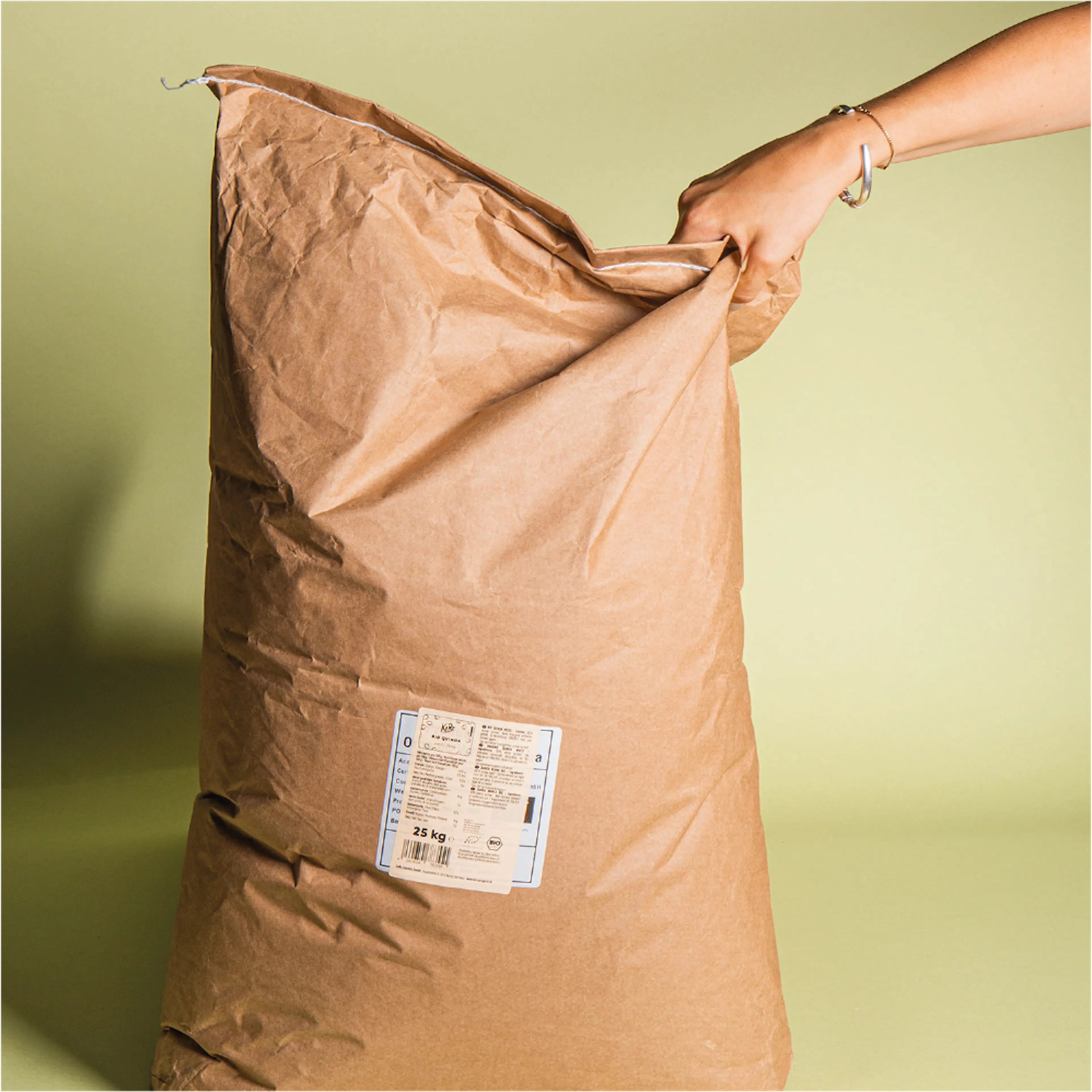 une personne tient un sac en papier brun avec une étiquette bleue qui indique 25 kg