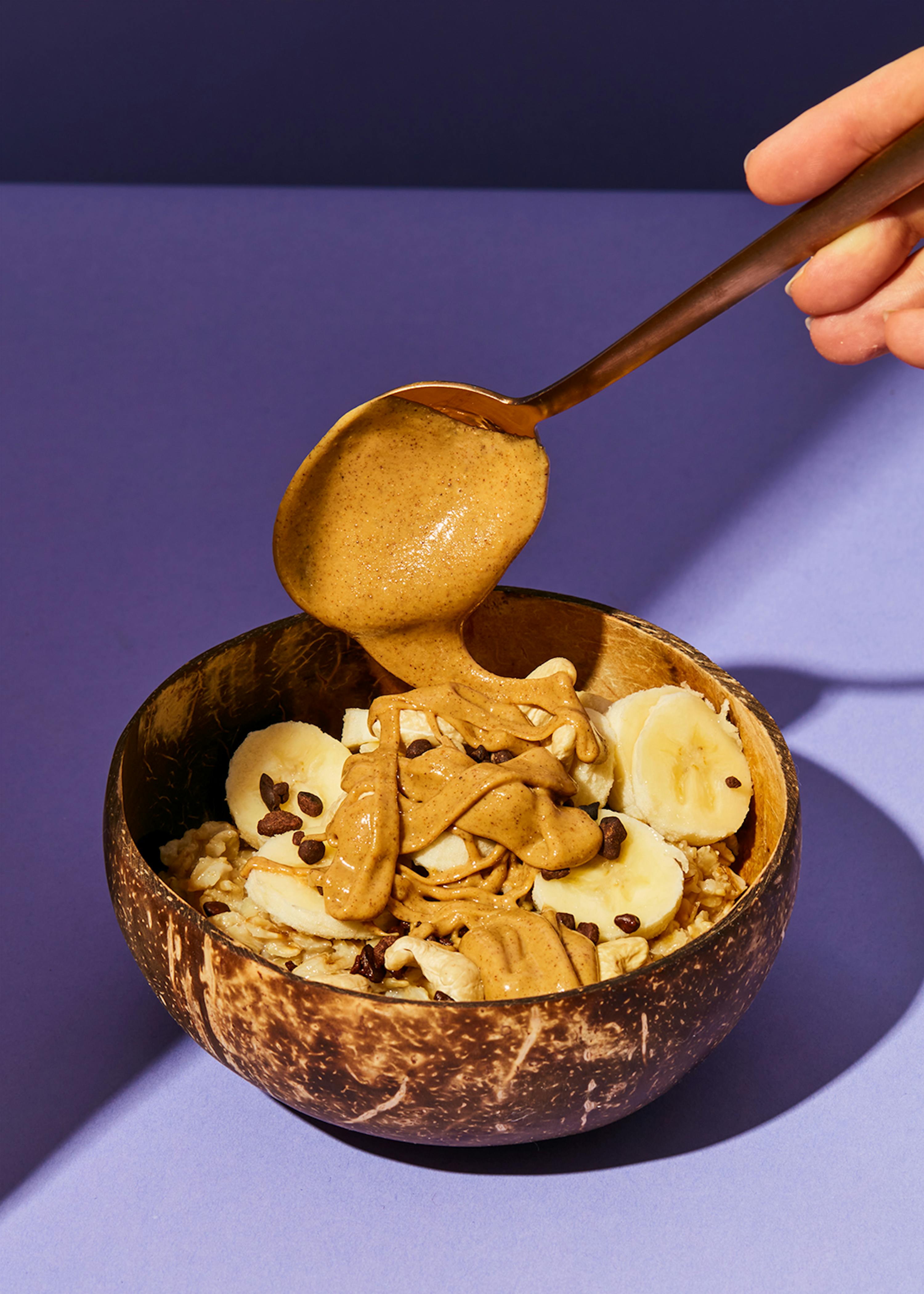 una persona versa burro di arachidi su una ciotola di cereali e banane
