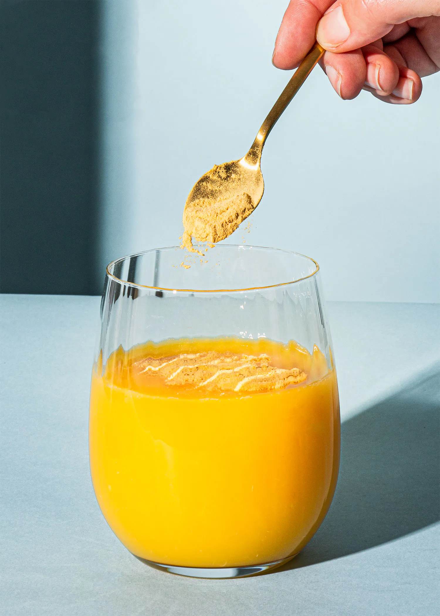 Eine Person gießt einen Löffel in ein Glas Orangensaft