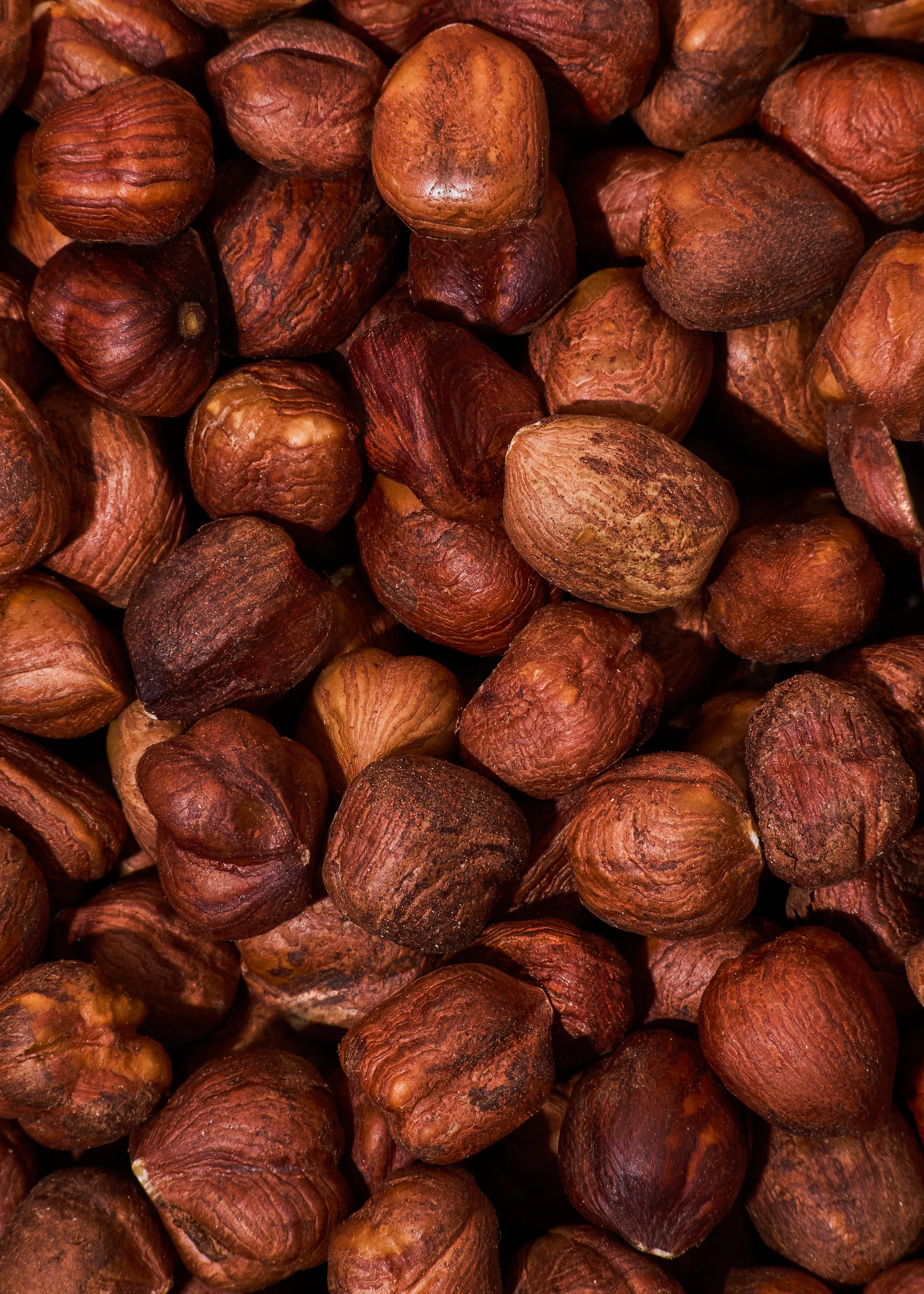 a close-up of many shelled hazelnuts, displaying their varied brown and reddish-brown colors and textured surfaces.