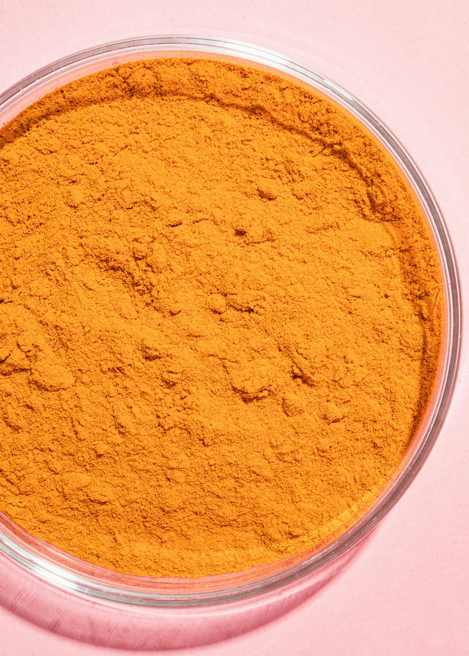 Organic ground turmeric 1kg a glass dish filled with orange powder on a pink background