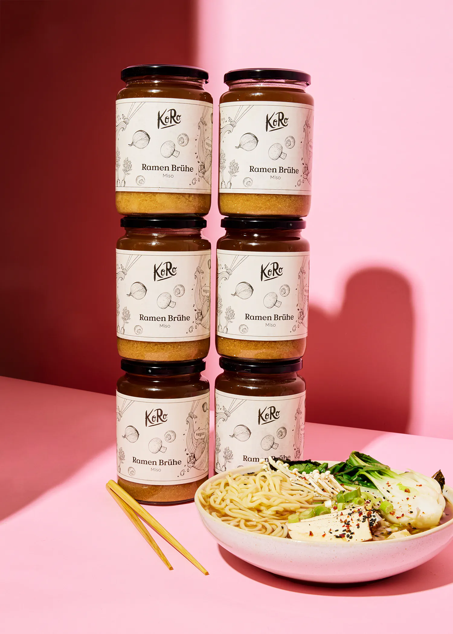 quatre bocaux de ramen broth sont empilés les uns sur les autres sur une table rose