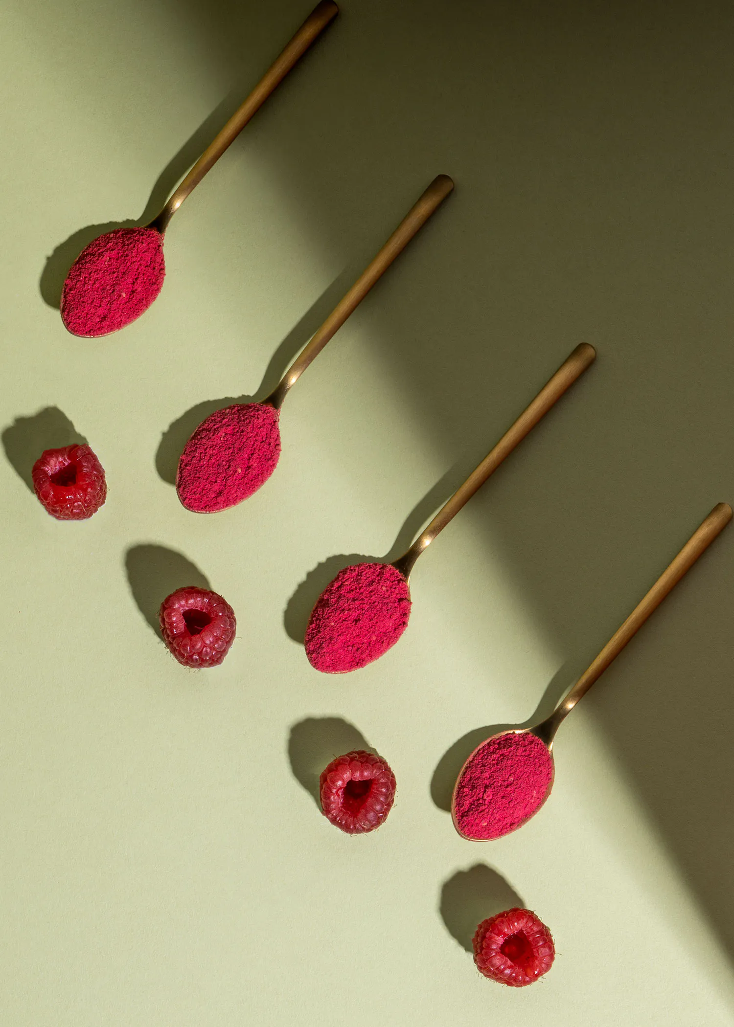 quatre cuillères remplies de poudre de framboise et de framboises sur une surface verte