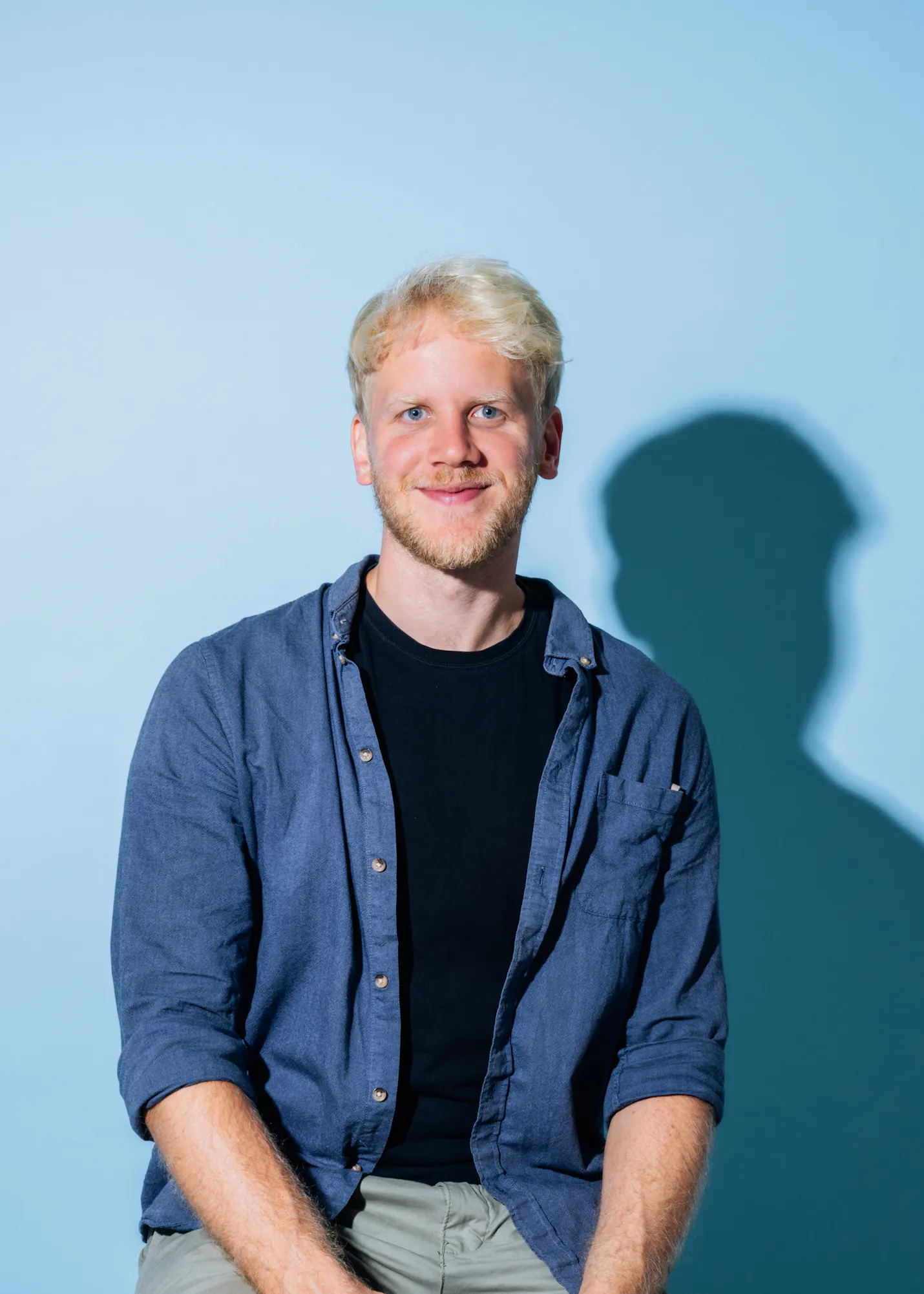 un homme avec une chemise bleue et un t-shirt noir sourit à la caméra