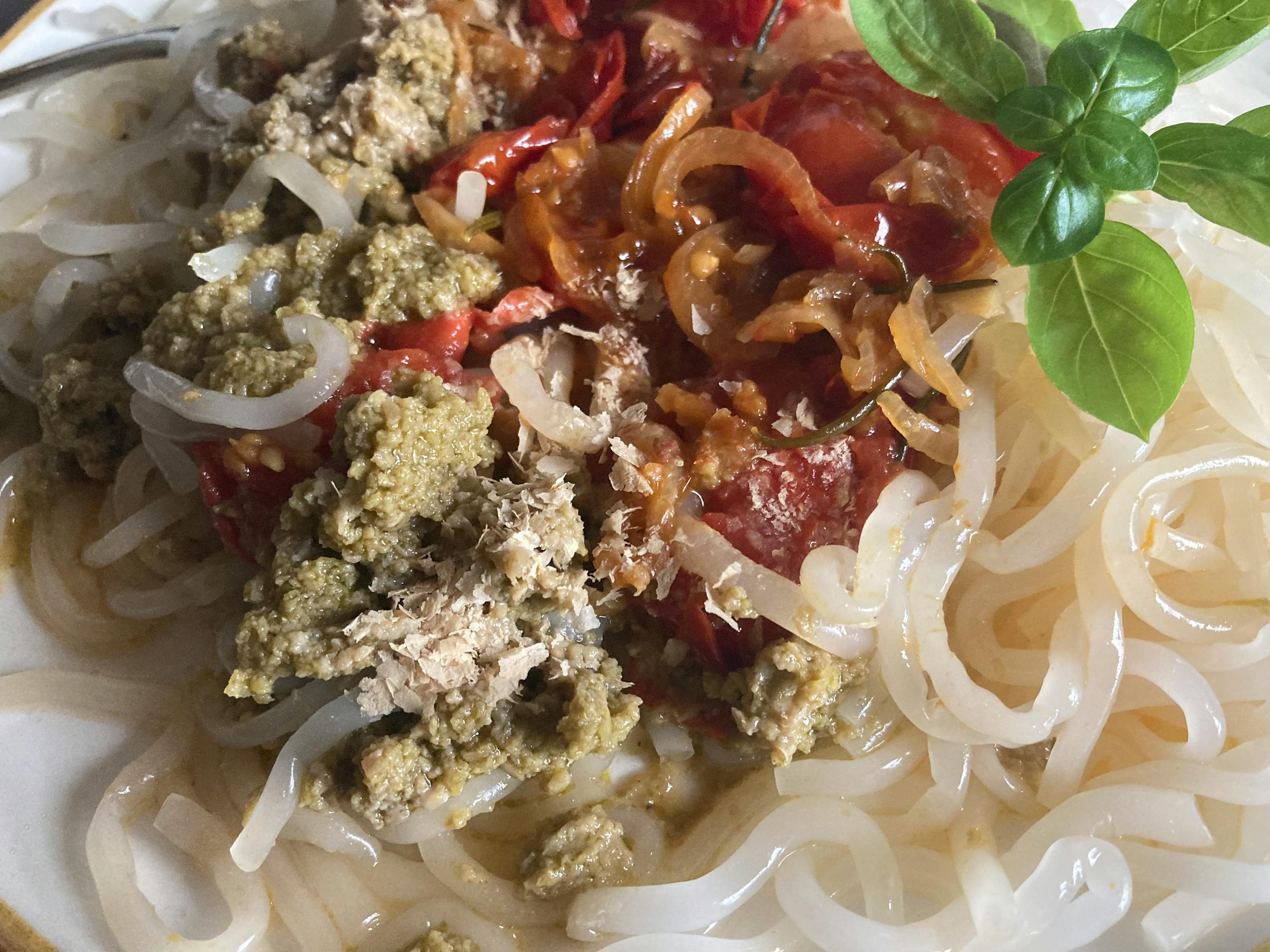 a plate of noodles with meat and tomatoes on top