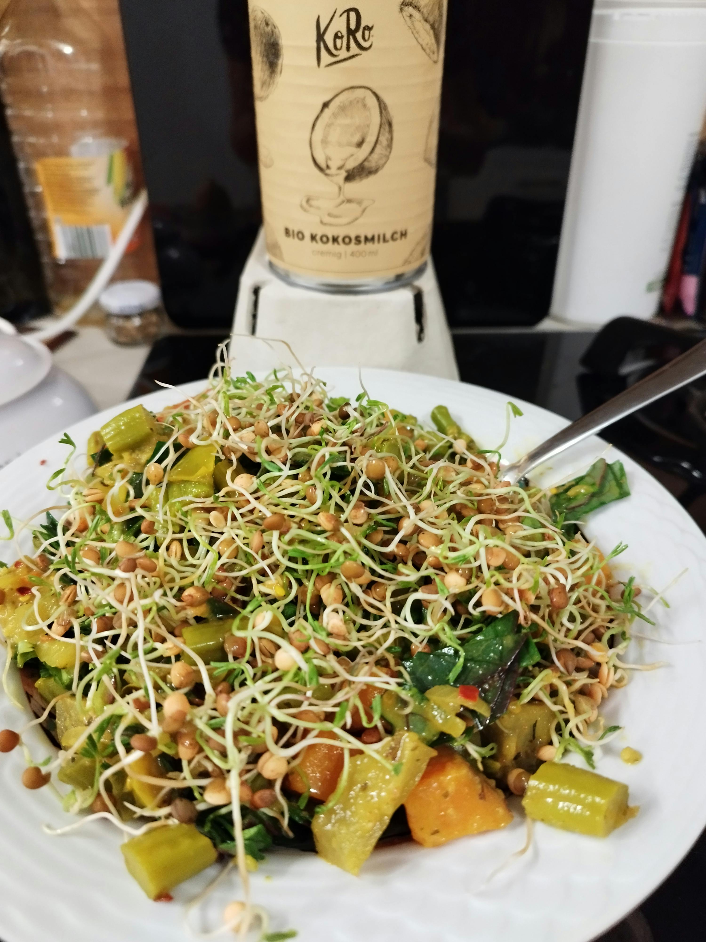 ein weißer Teller mit einem Salat und einer Flasche kokosmilch dahinter