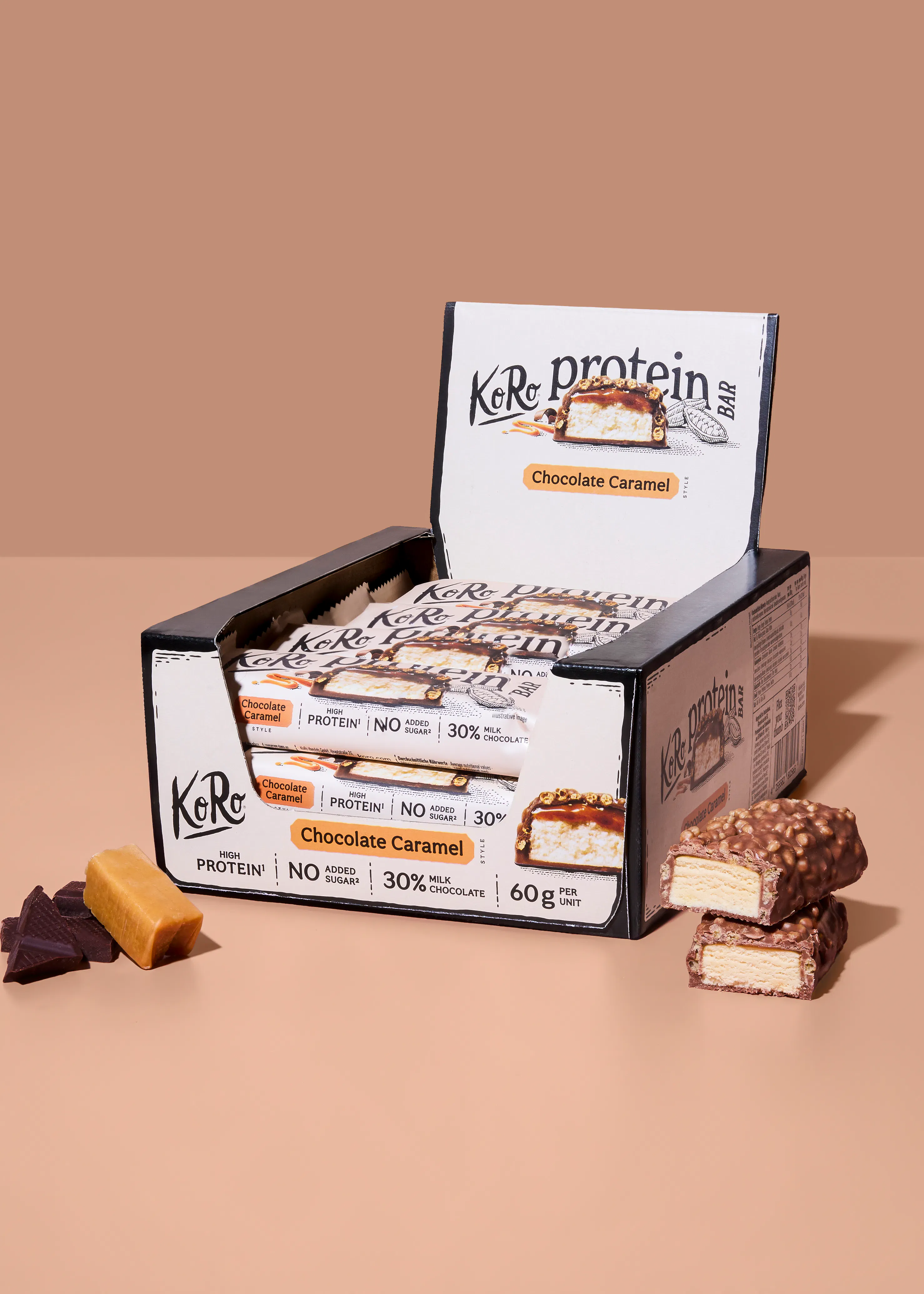 une boîte de présentation de barres protéinées koro saveur chocolat caramel, avec des barres déballées et coupées révélant l'intérieur, accompagnées de morceaux de chocolat et de caramel.