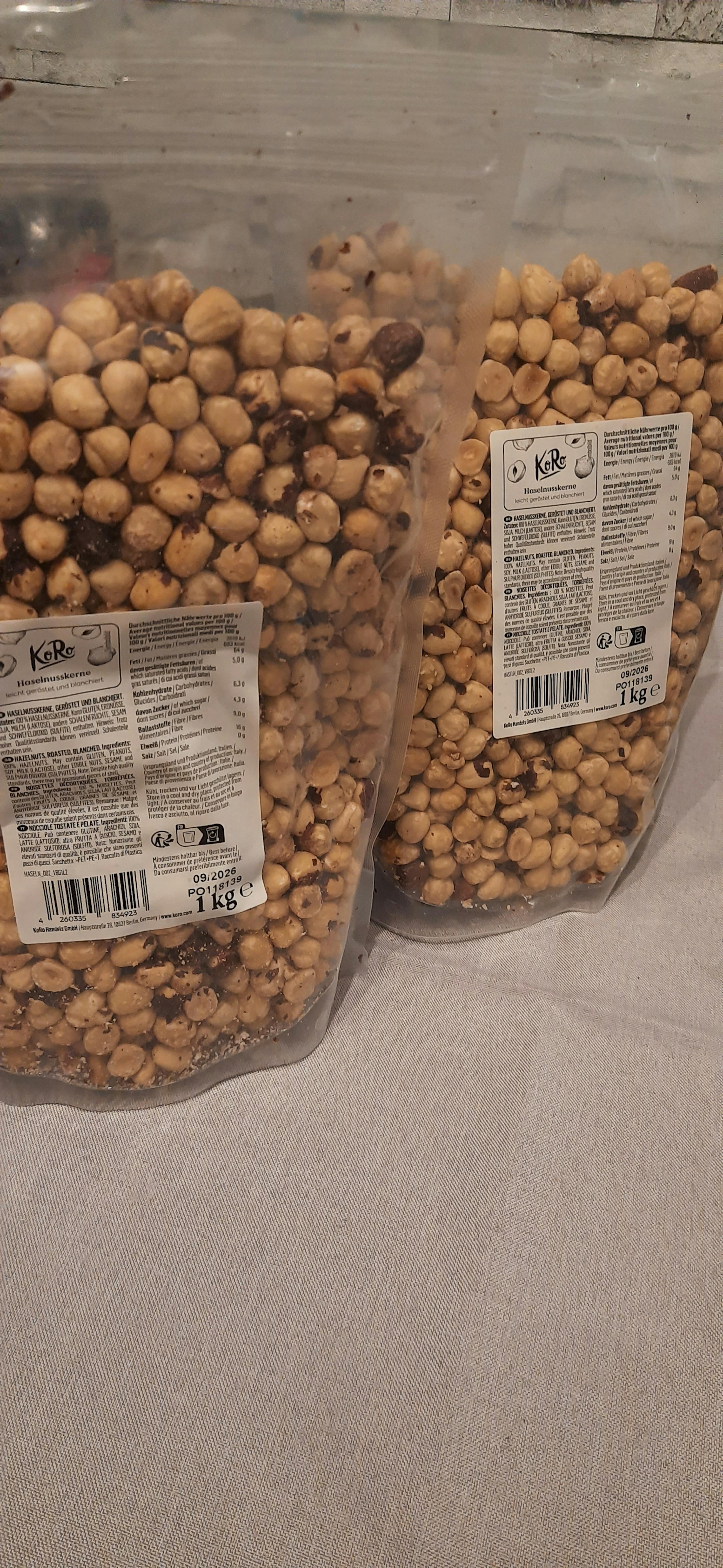 zwei transparente beutel mit gerösteten und blanchierten haselnusskernen der marke koro, jeweils 1 kg, liegen auf einer hellen oberfläche.