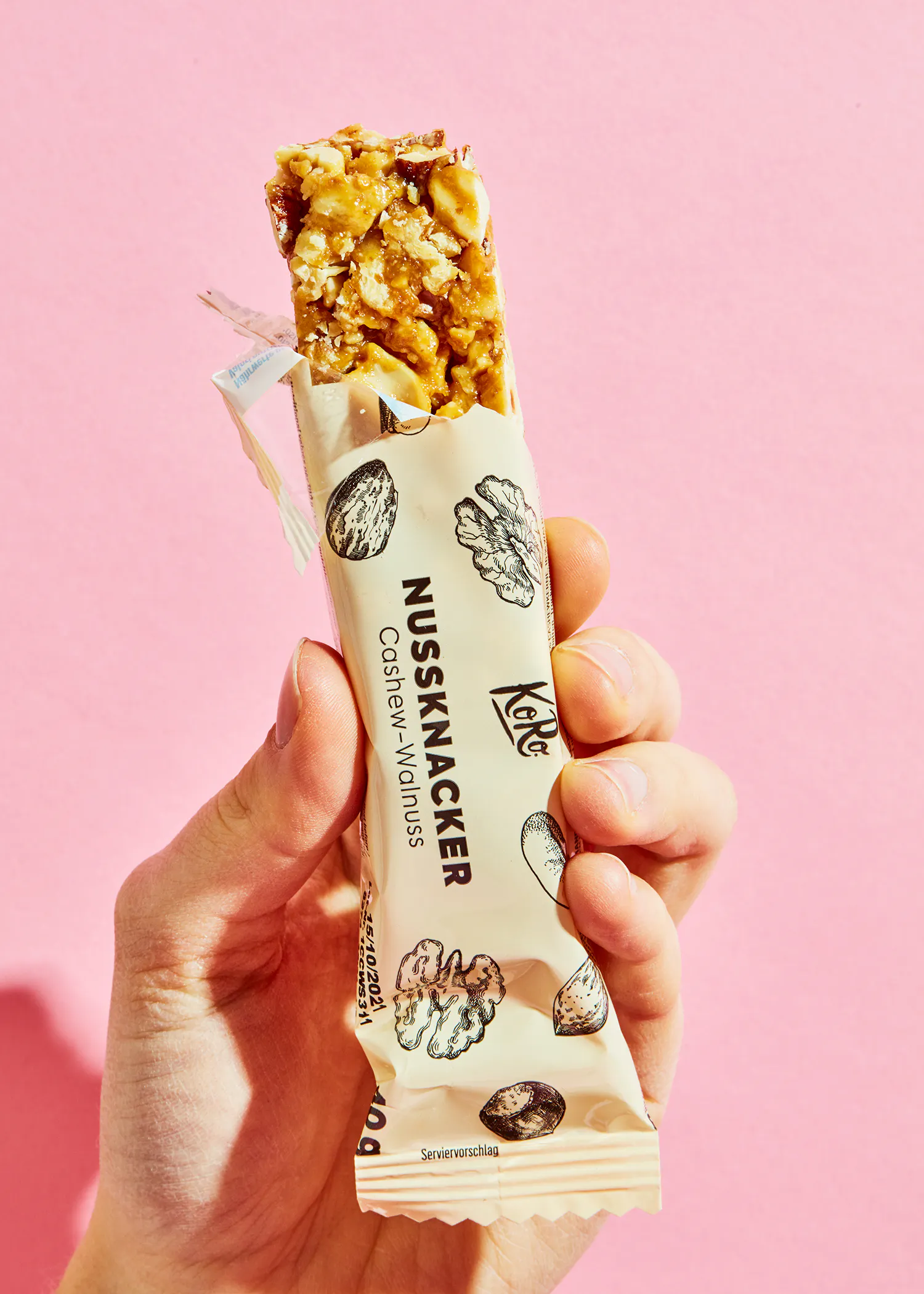 une personne tient une barre de céréales aux noix sur fond rose