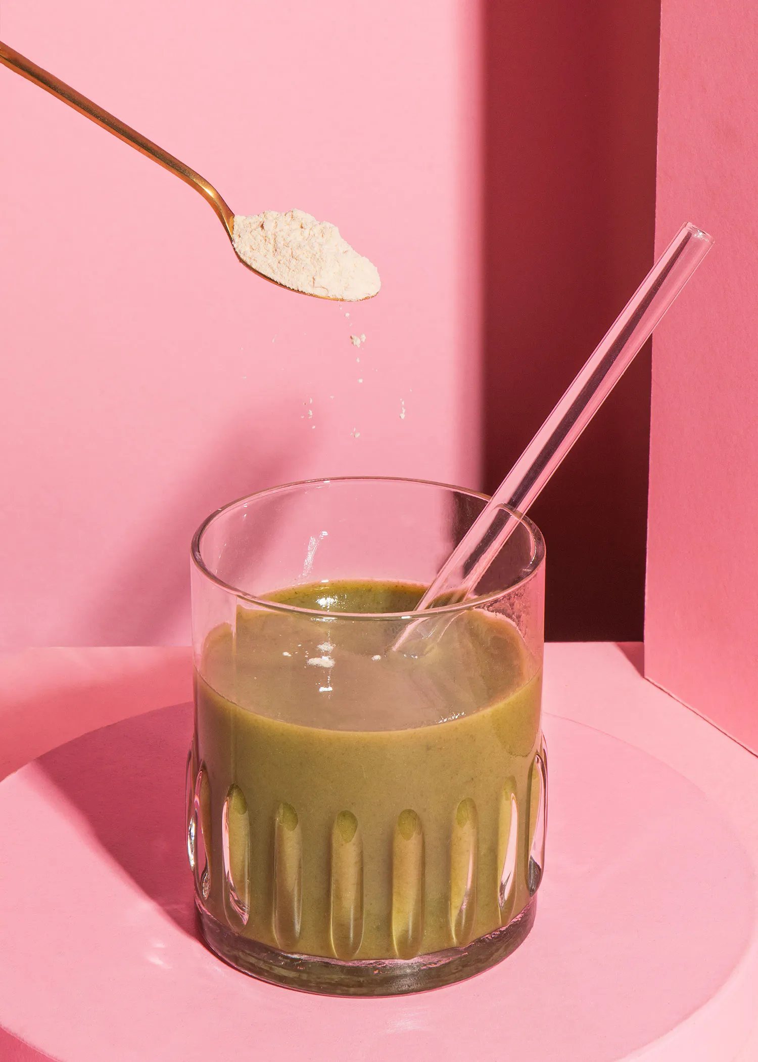 une cuillère de poudre est versée dans un verre de boisson verte avec une paille