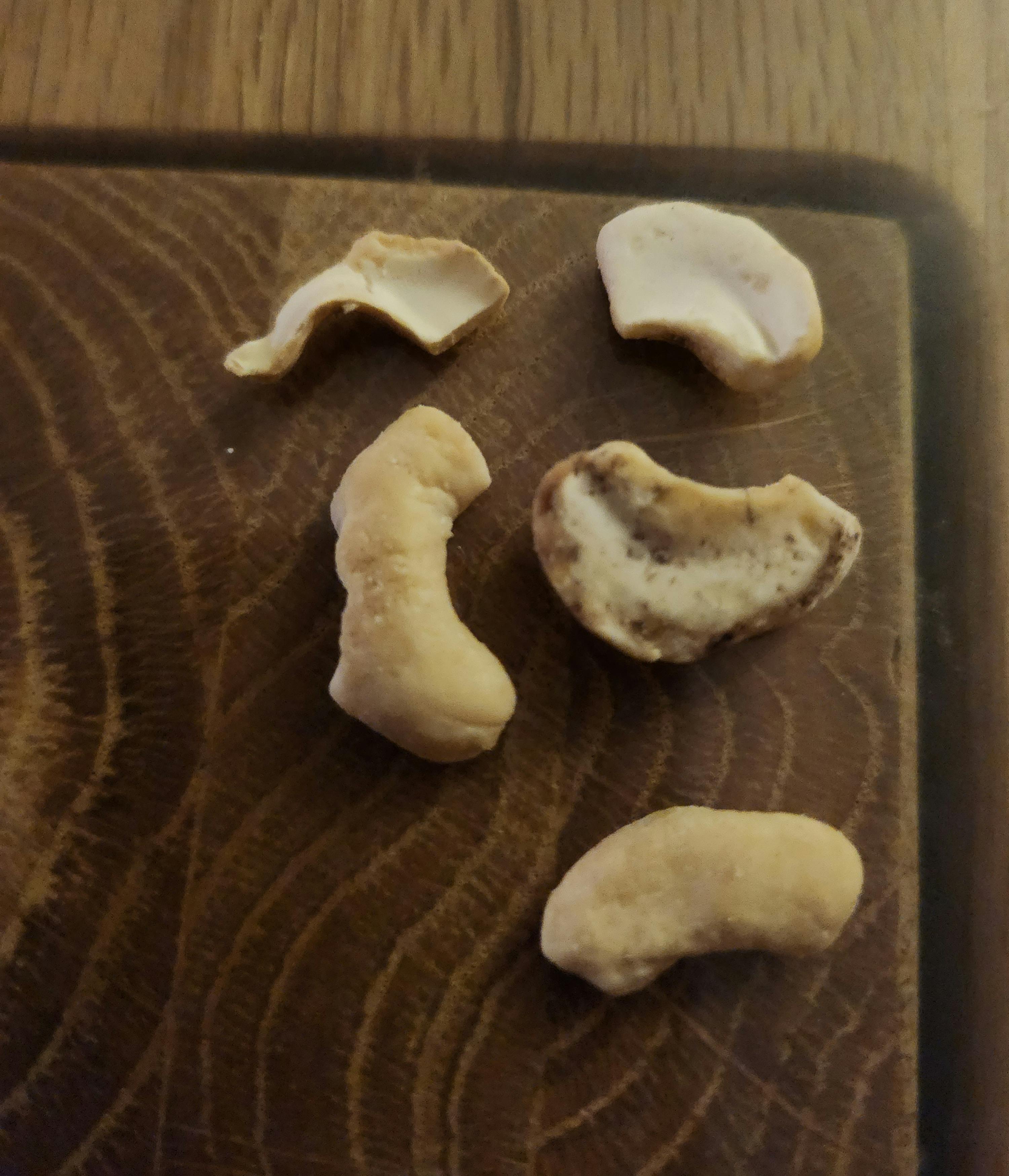 a wooden cutting board with cashews broken in half