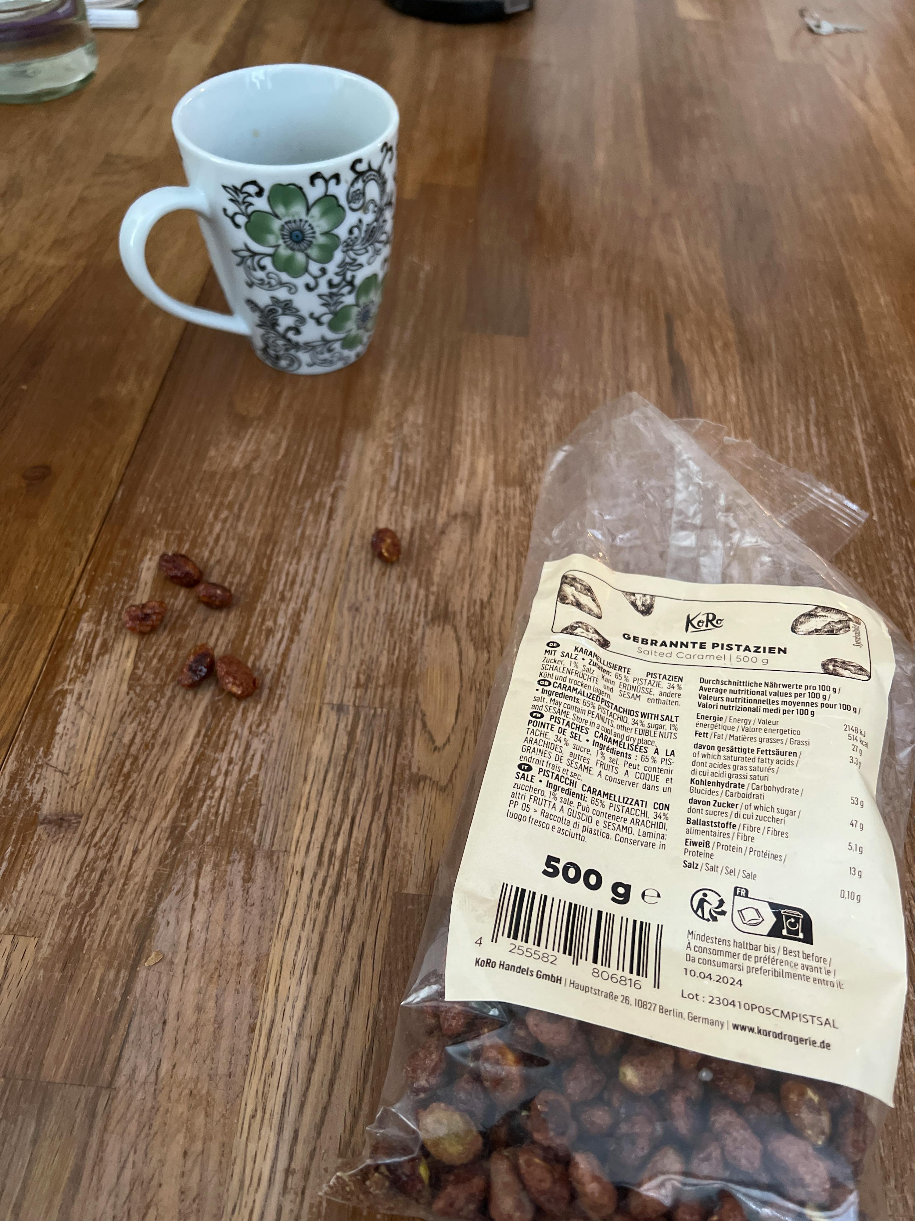 a bag of peanuts sits on a wooden table next to a mug