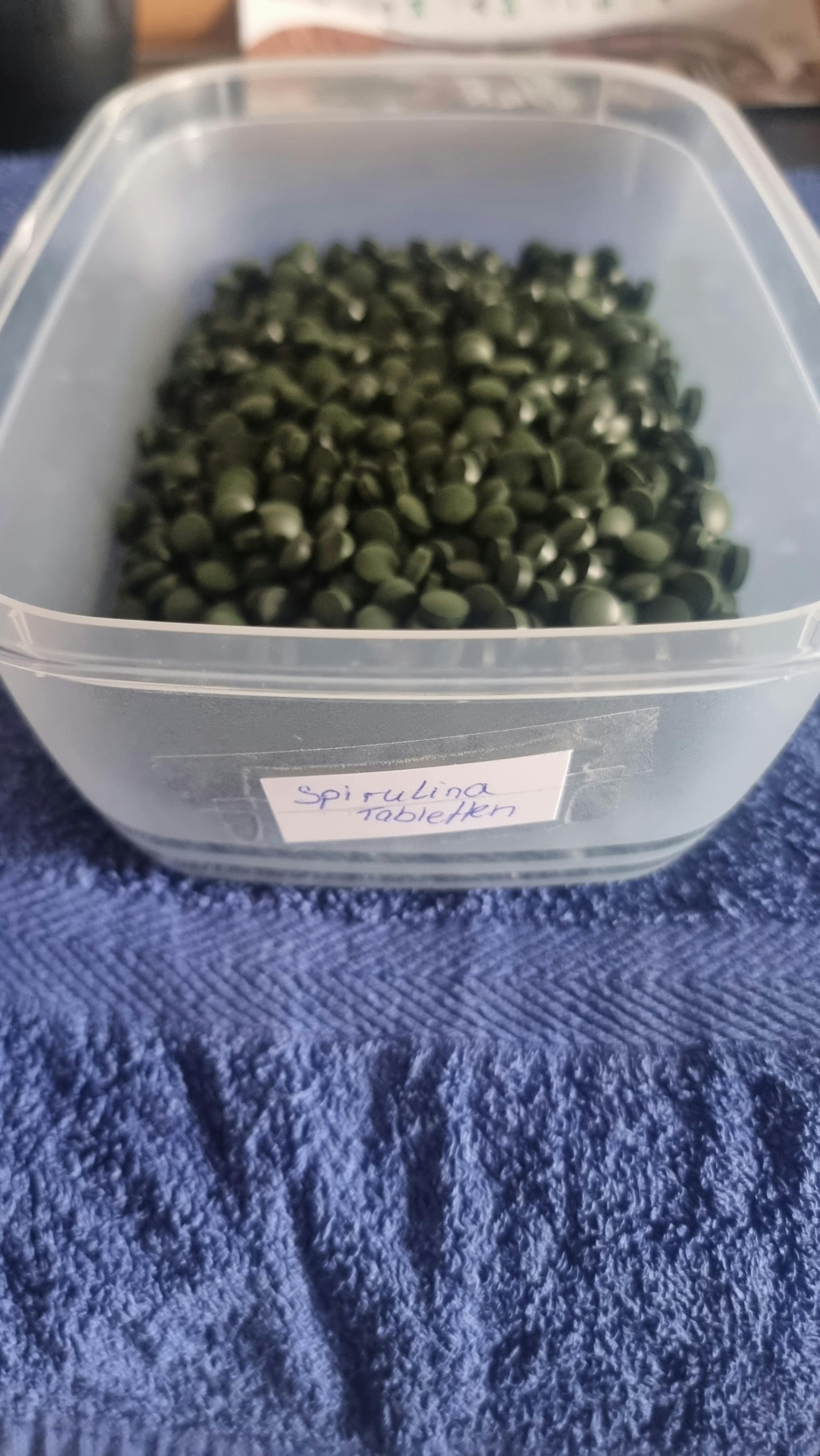 a plastic container filled with green pills with a label that says spirulina
