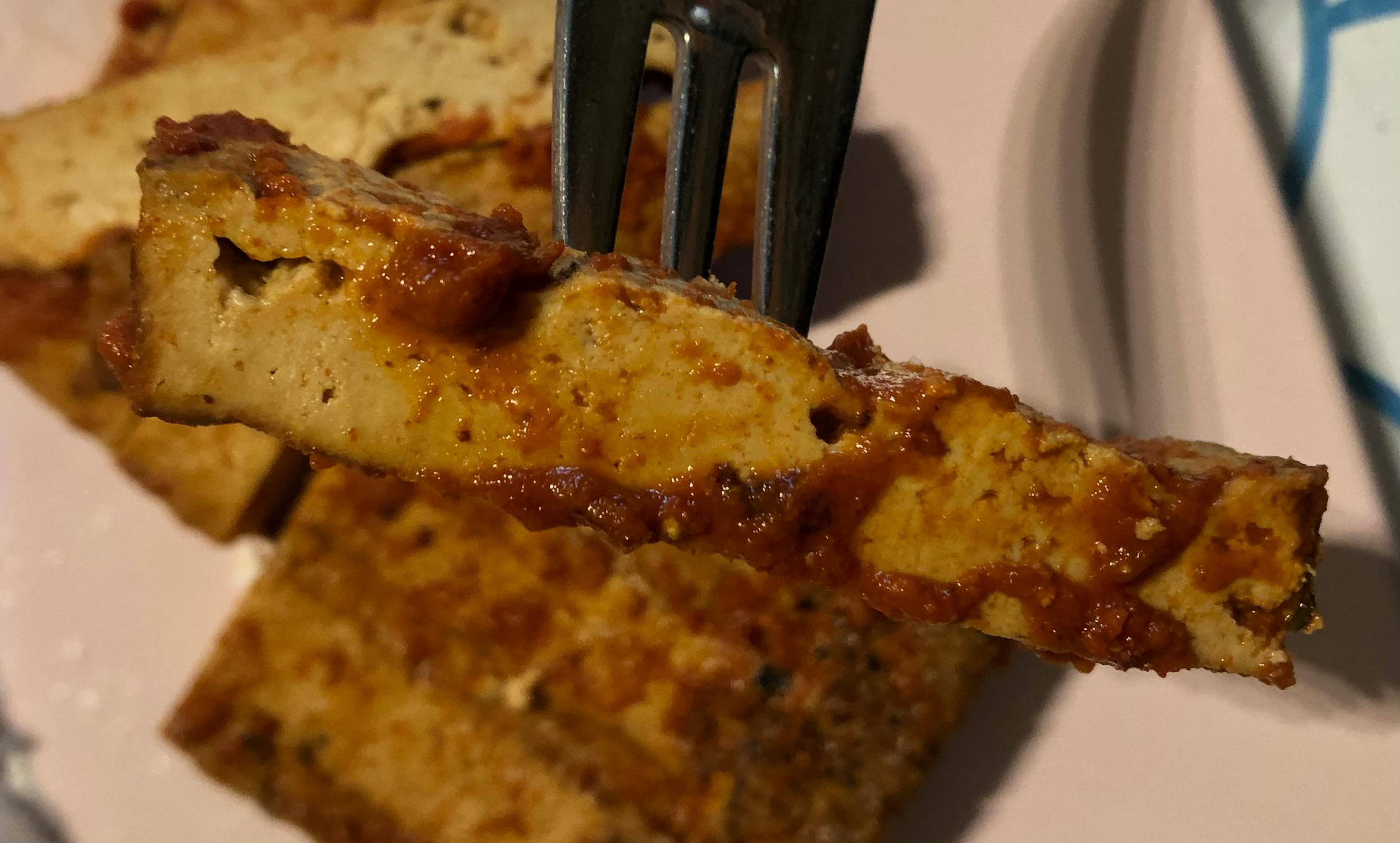 ein Stück tofu wird mit einer gabel auf einem rosa teller gegessen