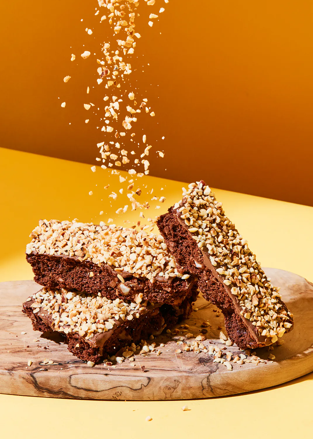 une planche à découper en bois avec des brownies et des noix tombant dessus