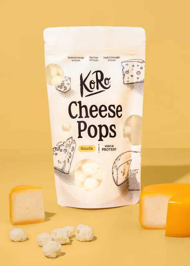 confezione di koro cheese pops al gouda circondata da pezzi di formaggio gouda e snack croccanti su sfondo giallo.