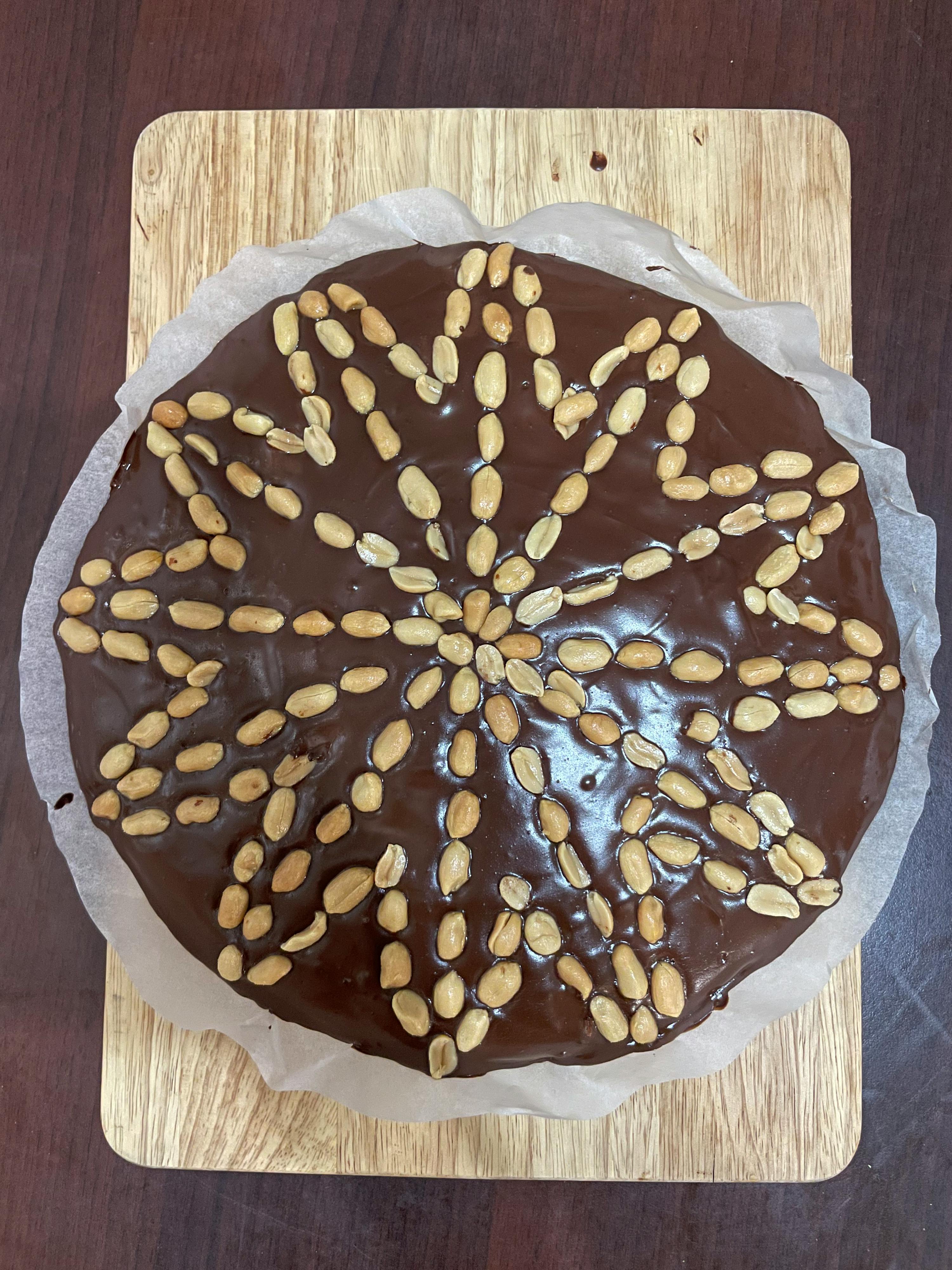 a chocolate cake with peanuts on it on a wooden cutting board