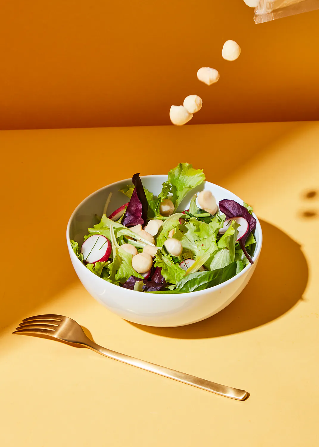 eine weiße Schüssel mit einem Salat und einer Gabel auf einem gelben Tisch