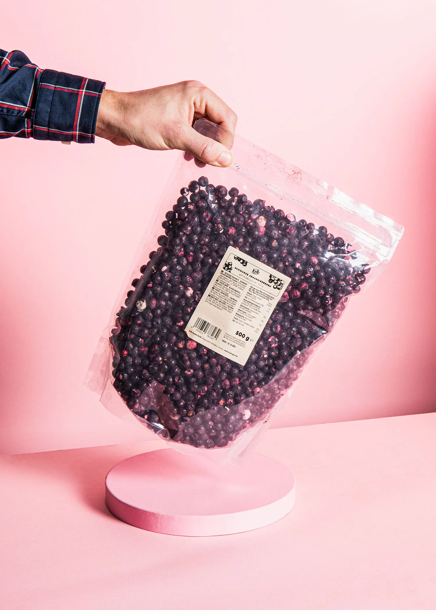 a person is holding a bag of blueberries on a pink background