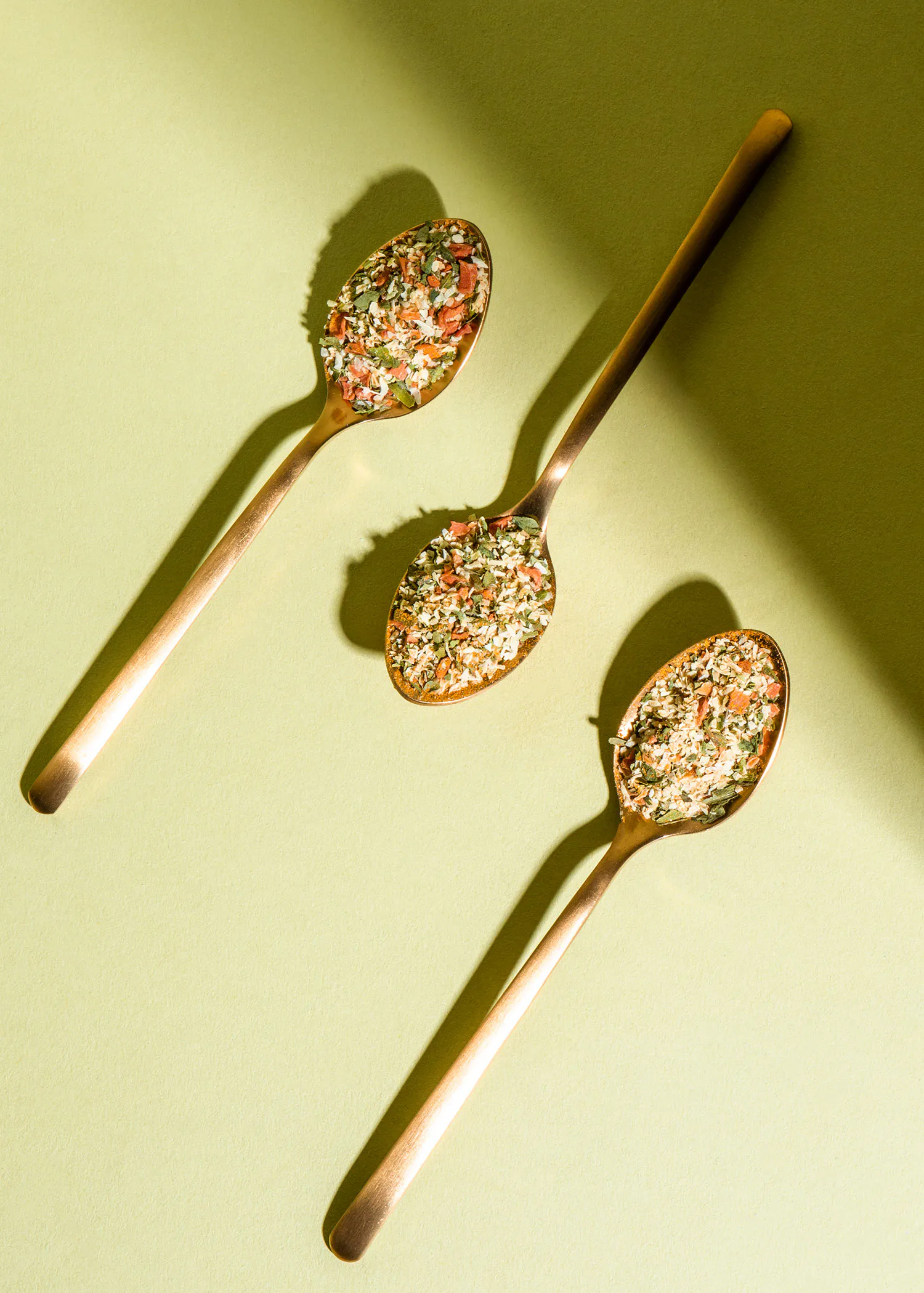 three spoons filled with different types of spices on a green surface