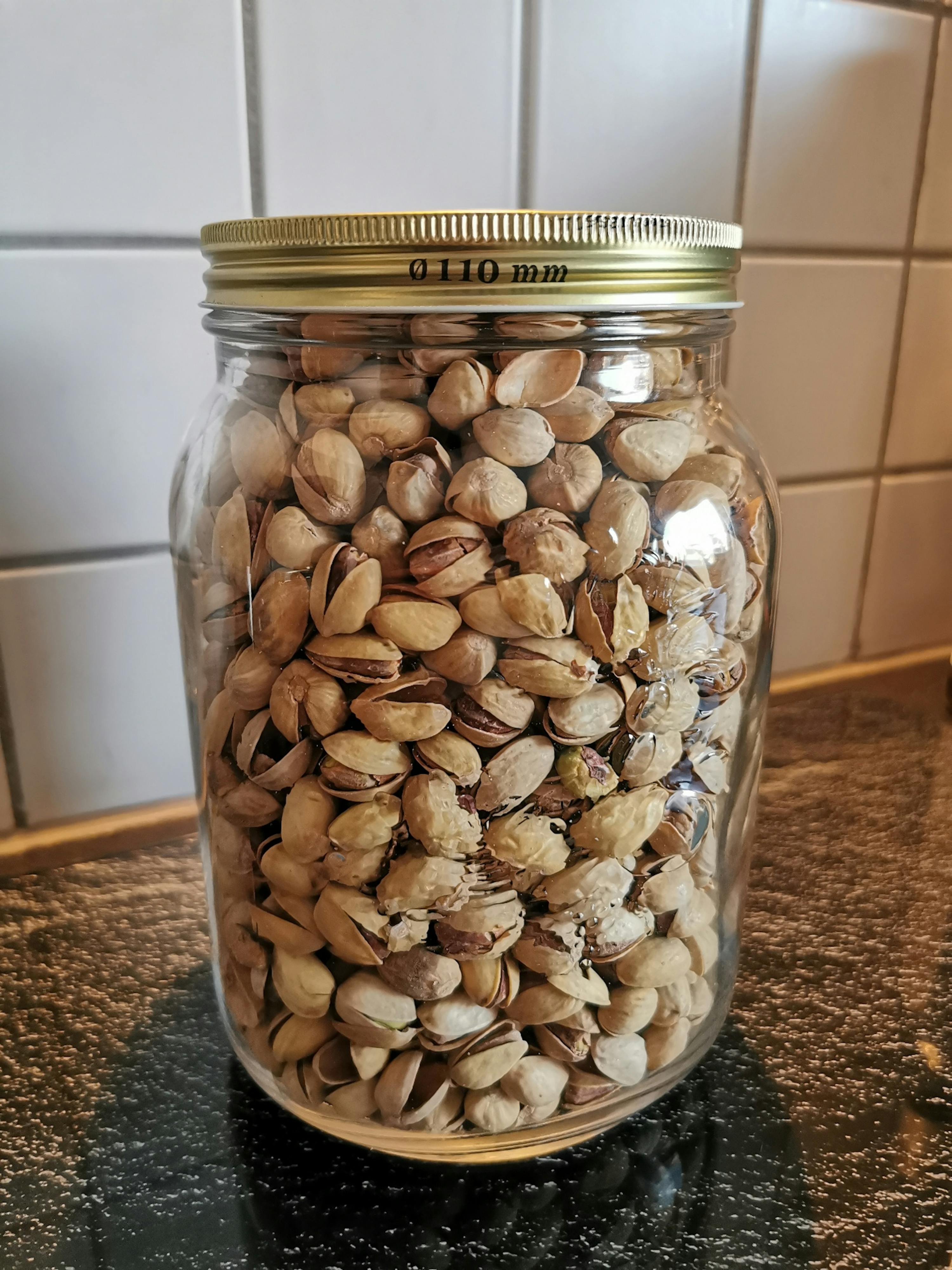 ein Glas gefüllt mit pistazien steht auf einer schwarzen Oberfläche