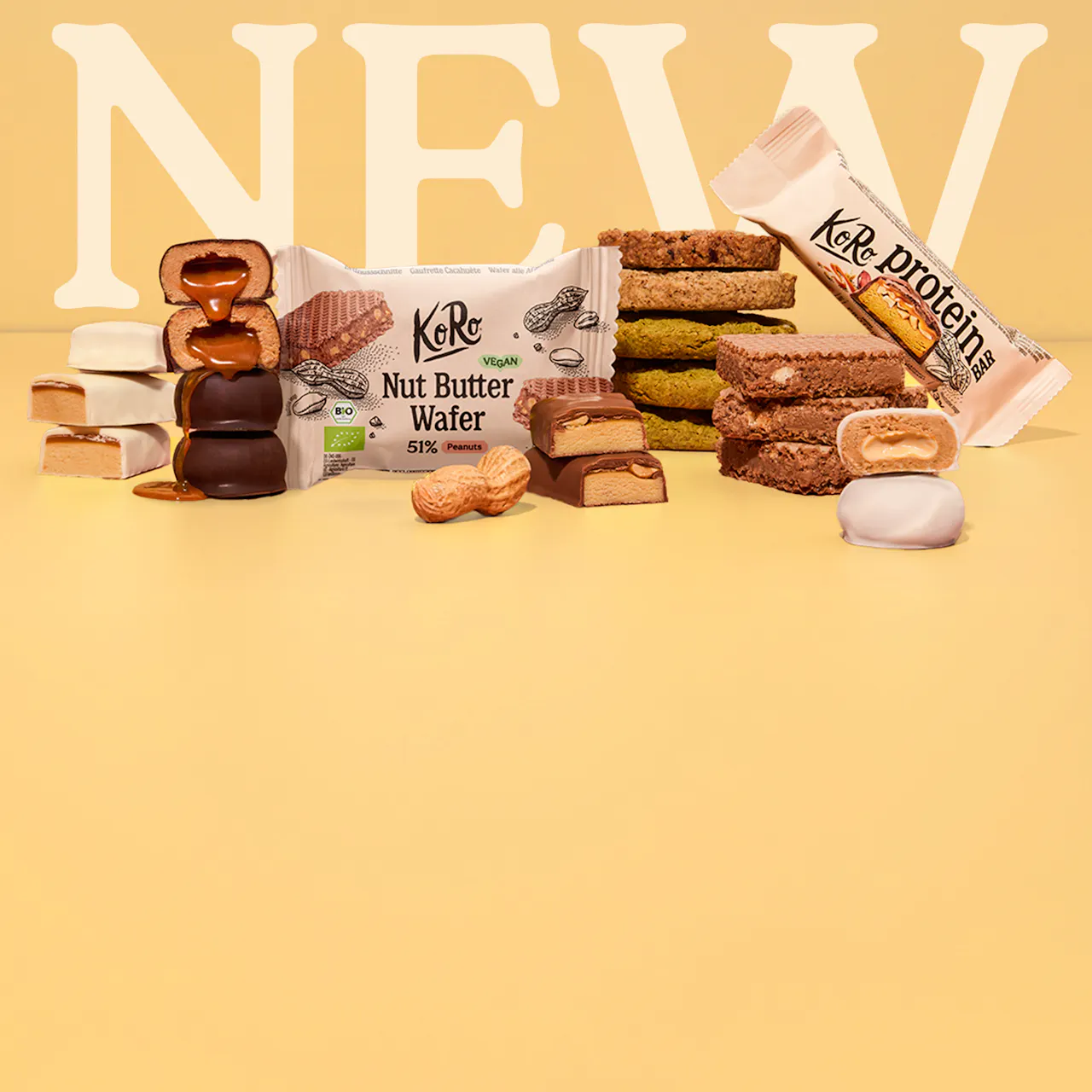 eine auswahl an koro-snacks wie nut butter wafer, proteinriegel und schokoladenkonfekt vor einem hellgelben hintergrund mit dem schriftzug new.