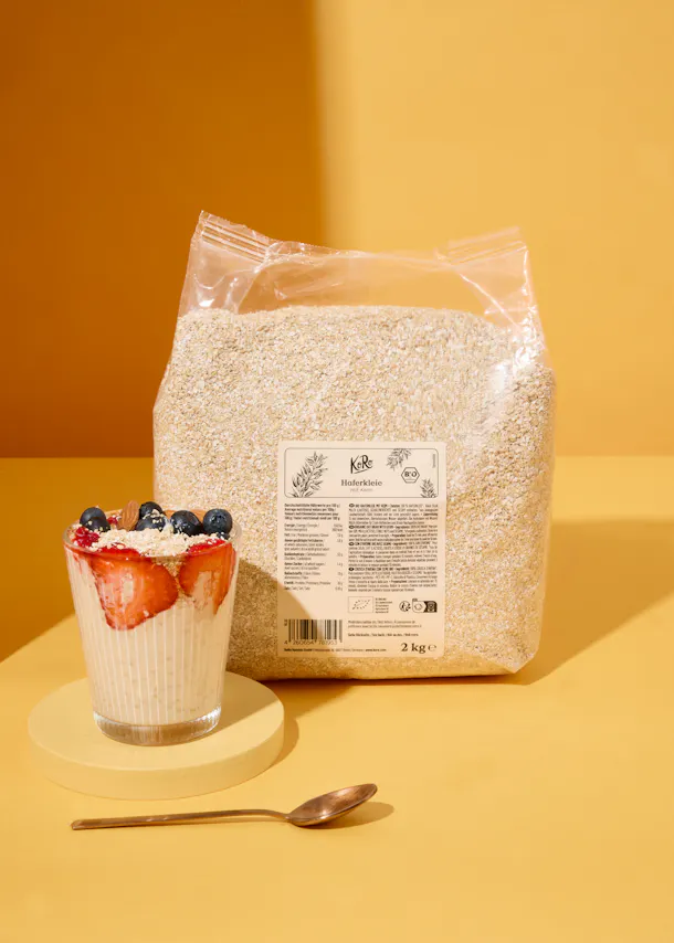 Eine Tüte Haferflocken steht neben einem Glas Haferflocken mit Erdbeeren und Blaubeeren