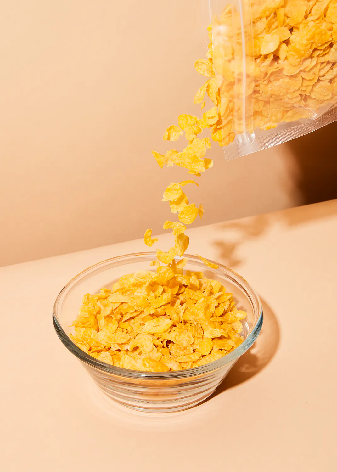une personne verse des flocons de maïs dans un bol en verre