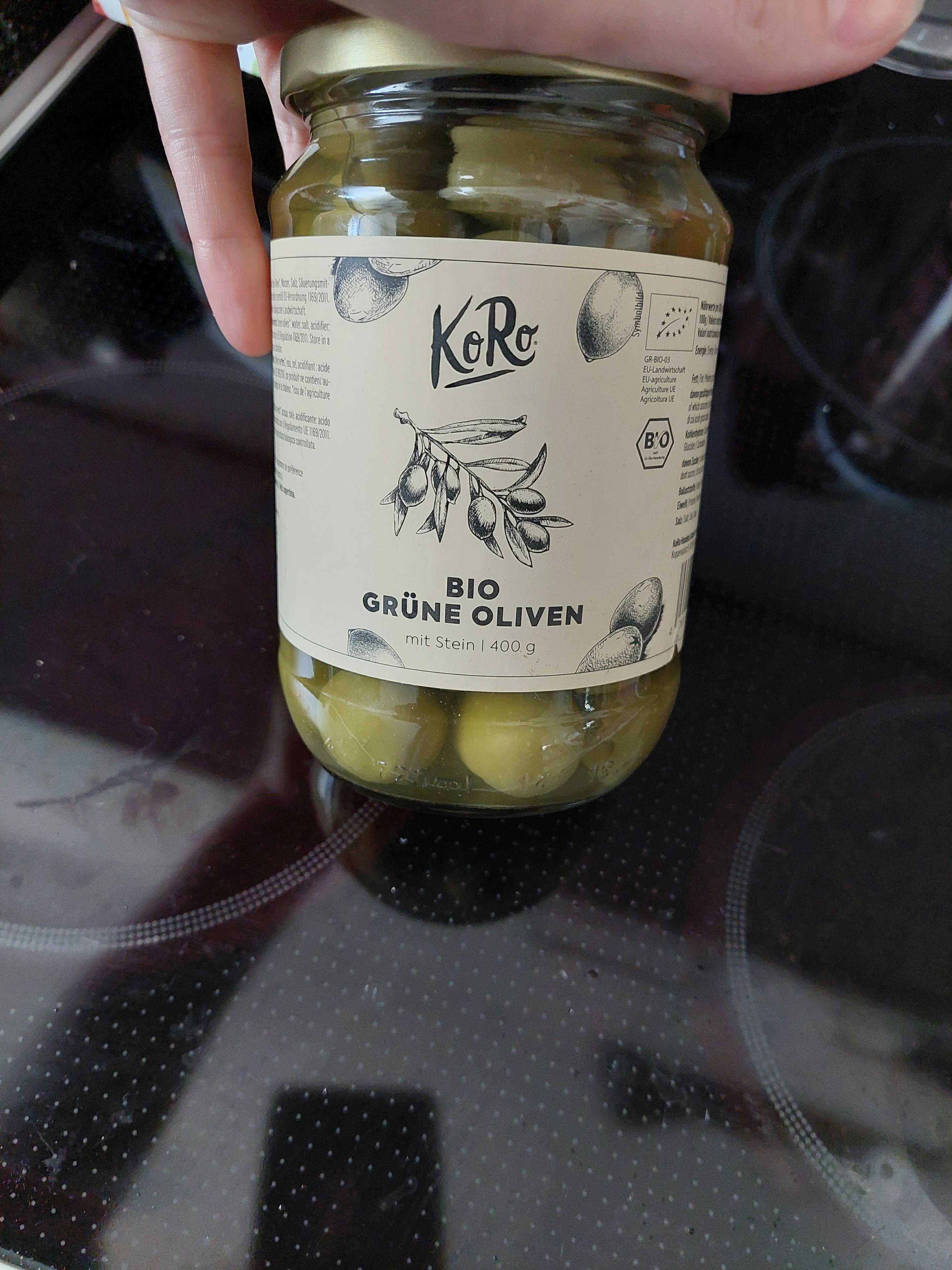 a person is holding a jar of green olives with a label that says bio grune oliven