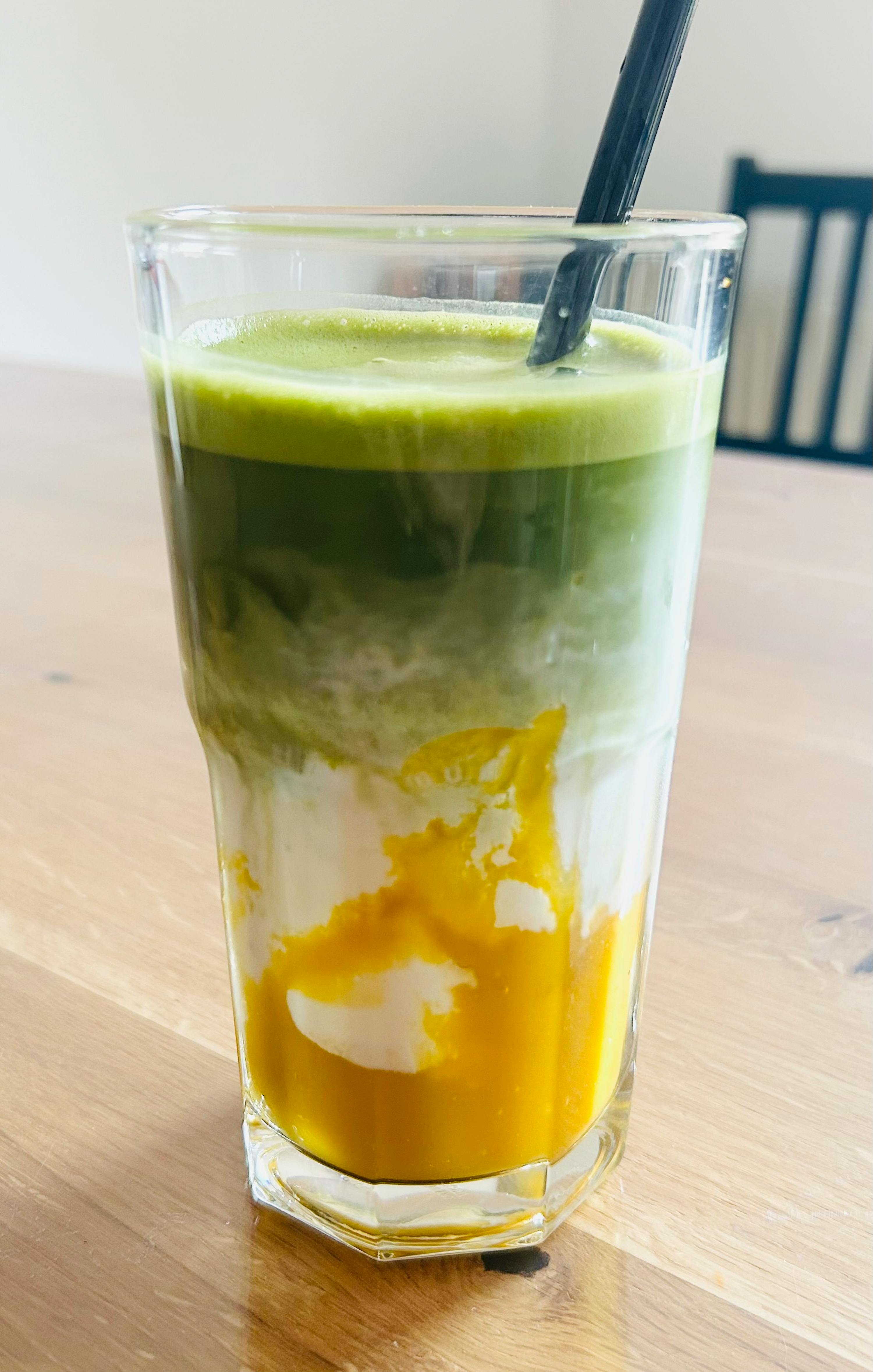 a glass of green and yellow drink with a black straw