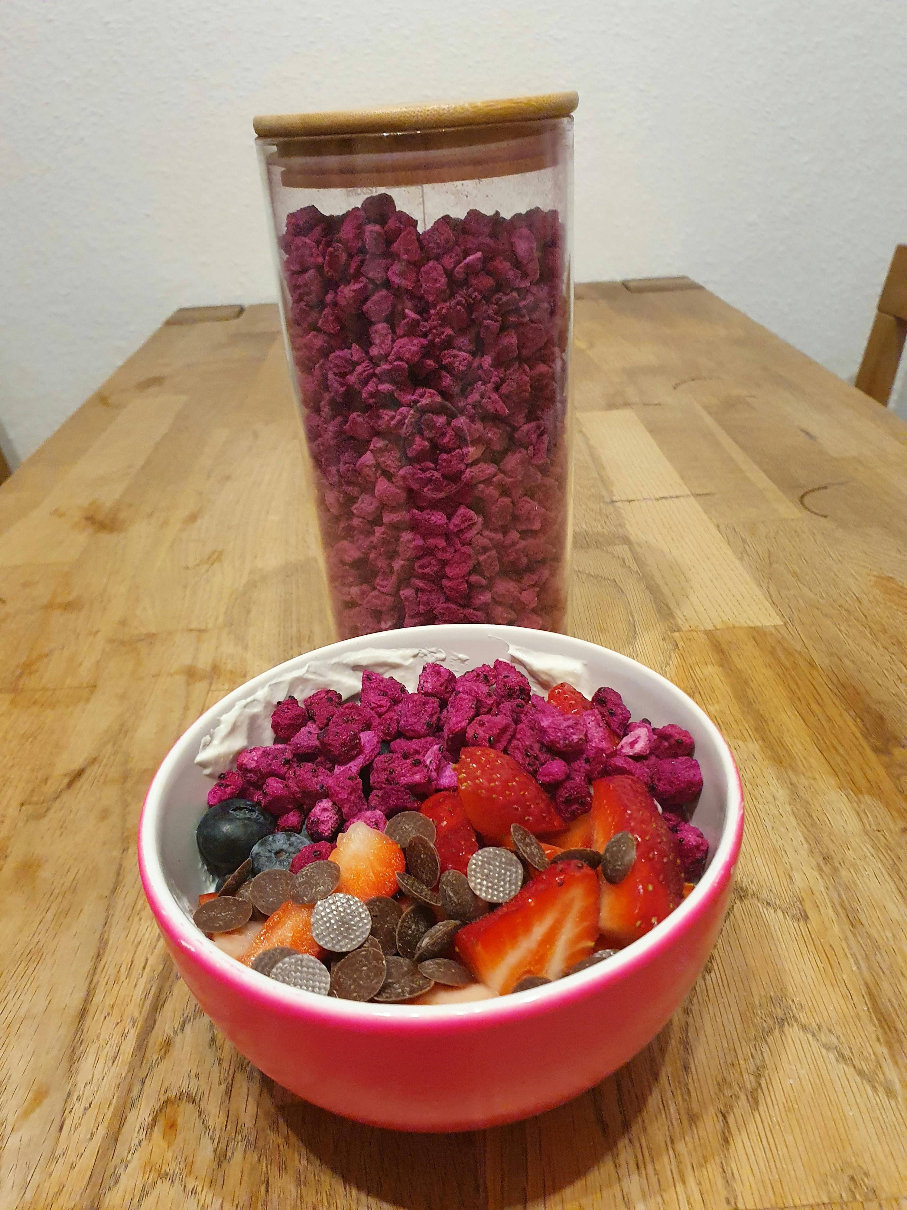 un bol rose rempli de fruits et de chocolat est assis sur une table en bois