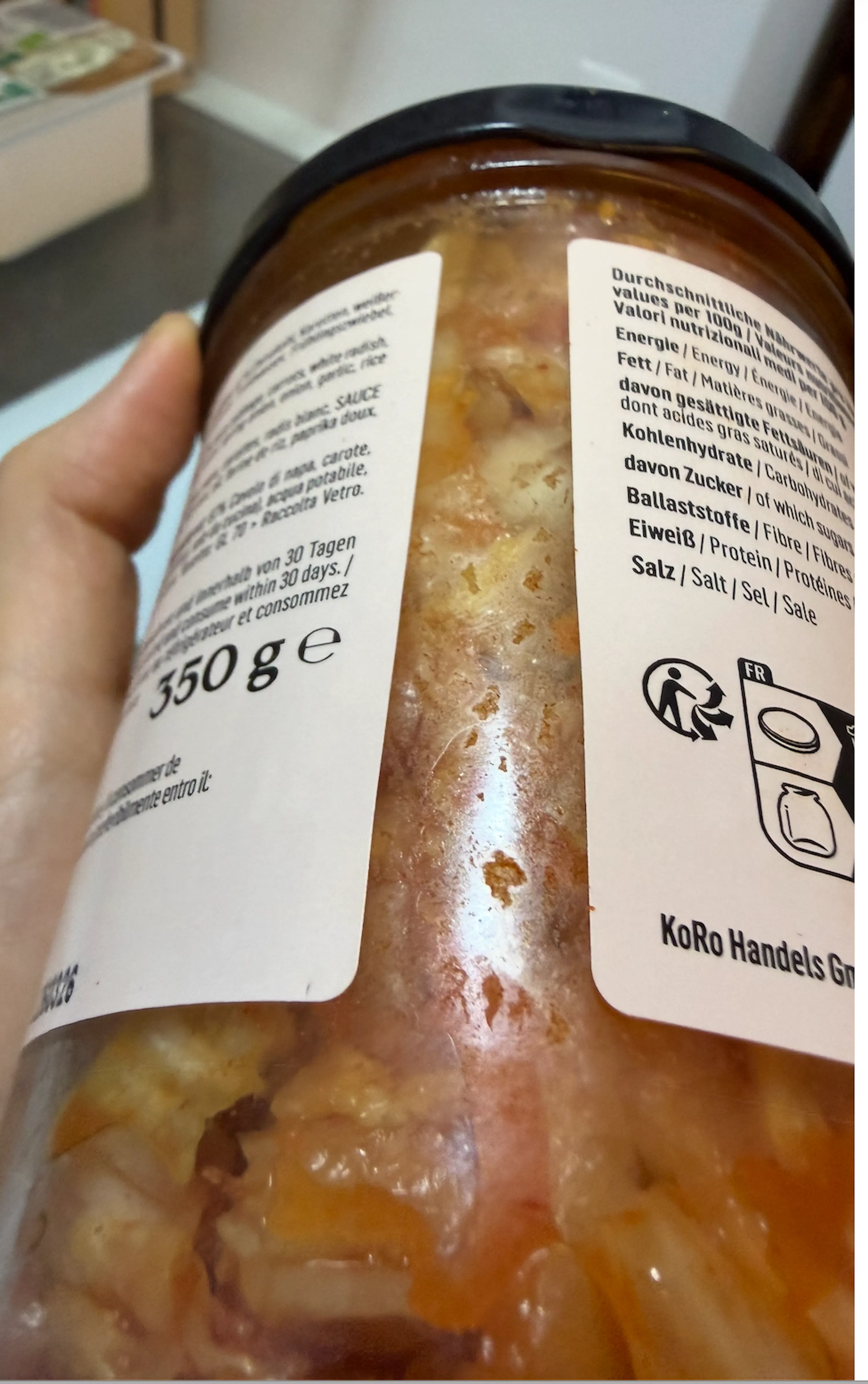 eine hand hält ein glasgefäß mit einer rötlich-orangen lebensmittelmischung, auf dessen etikett nährwertangaben, zutaten und das gewicht von 350 gramm sowie recyclesymbole zu sehen sind.