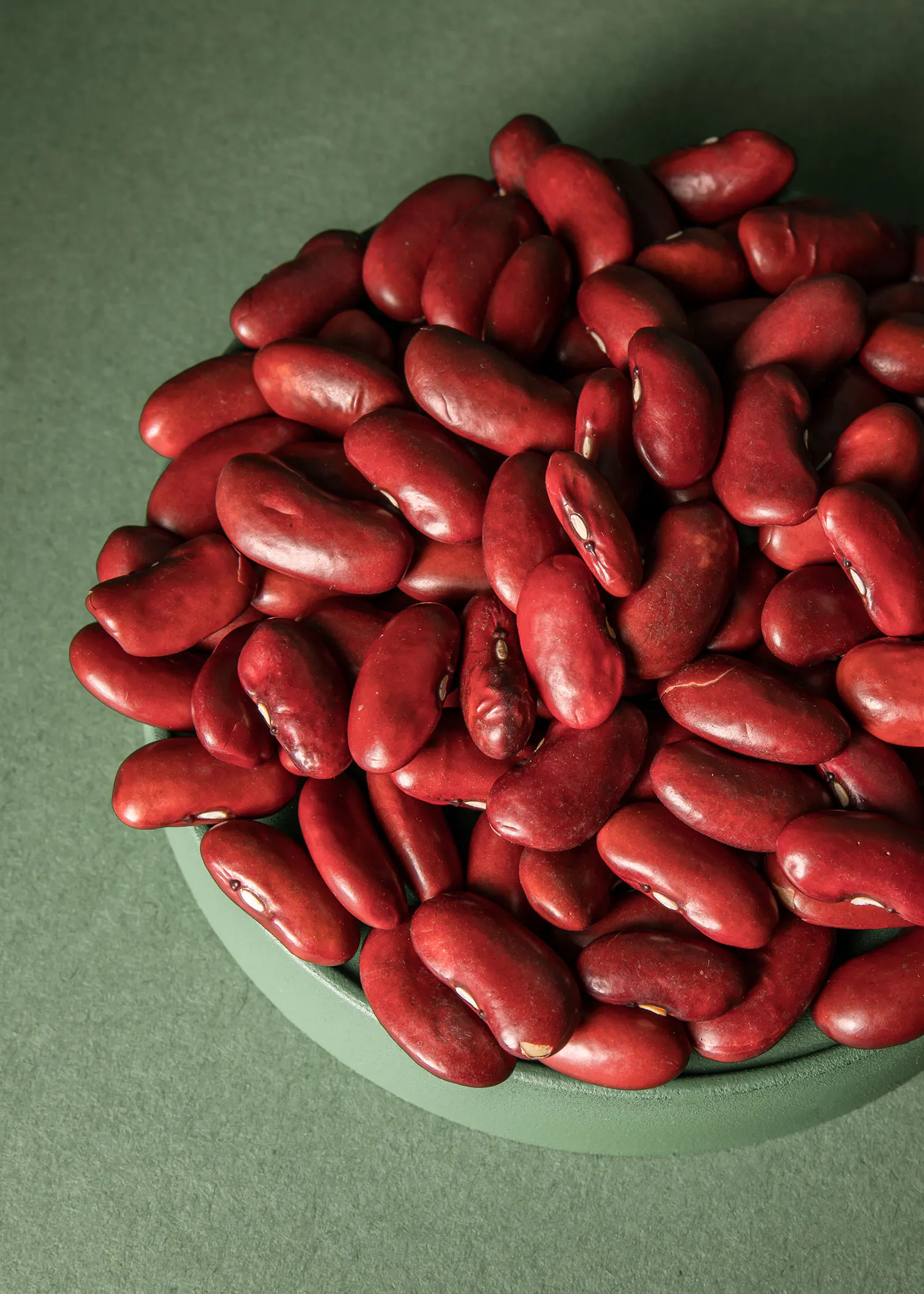 un bol vert rempli de haricots rouges sur une table verte