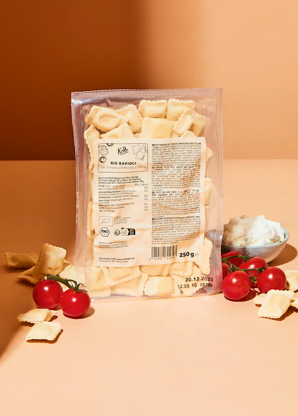 a bag of ravioli sits on a table with tomatoes and cheese