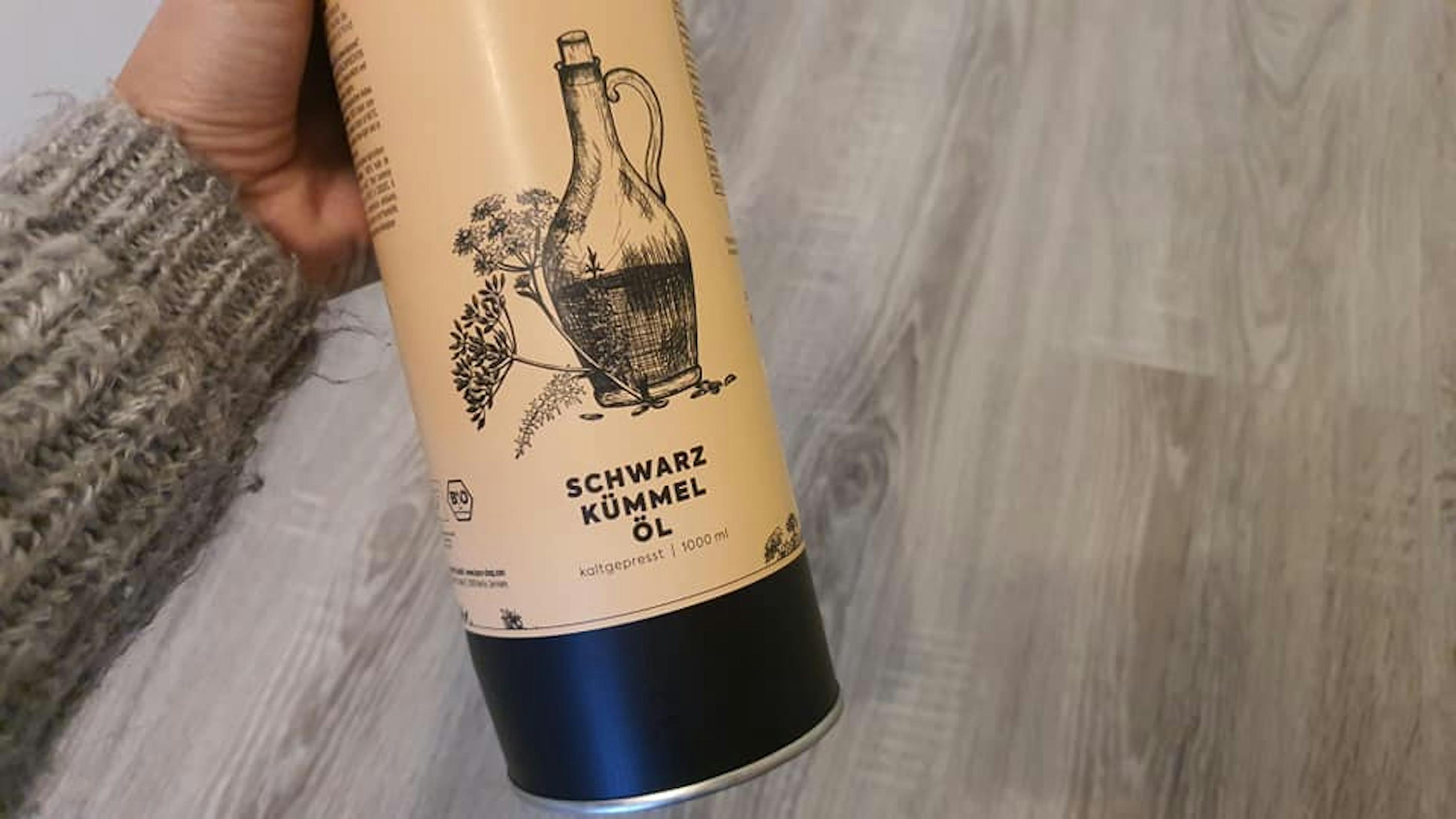 eine Person hält eine Dose schwarzkümmelöl in der Hand