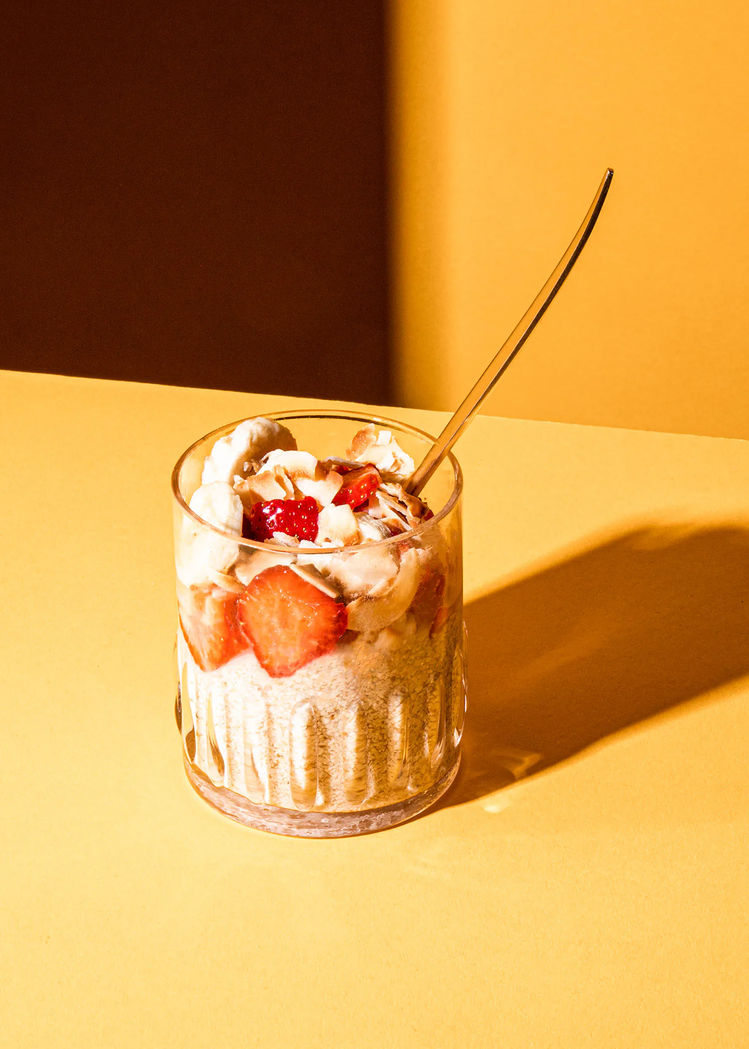 ein Glas mit Erdbeeren und Schlagsahne mit einem Löffel darin