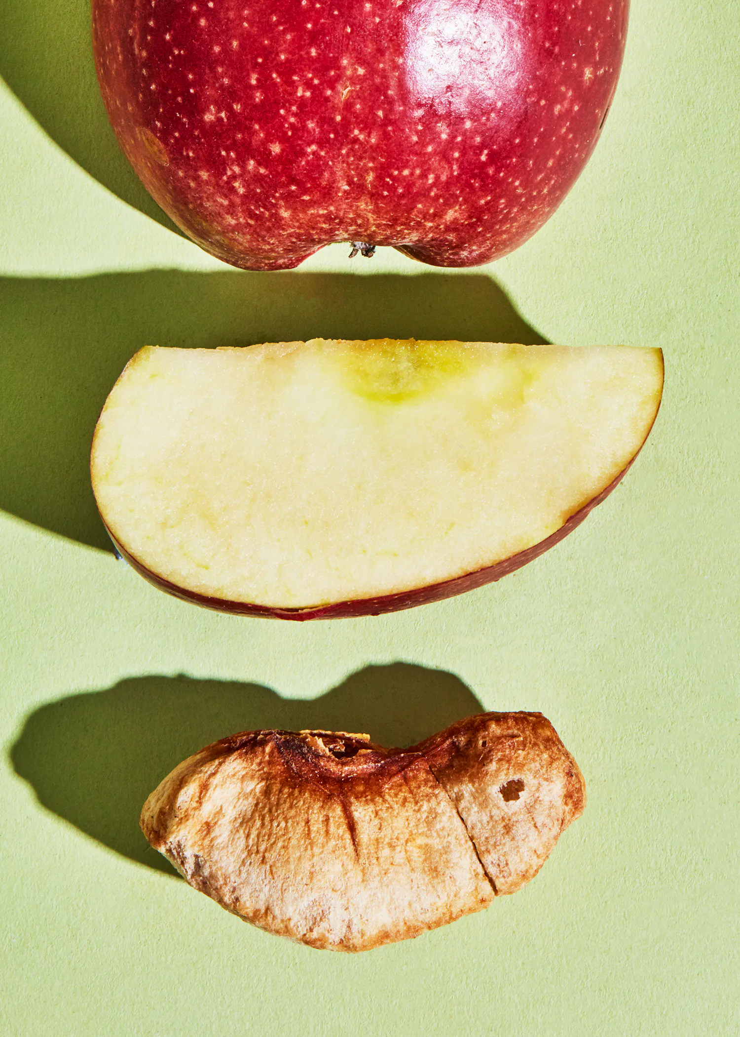 une pomme rouge est coupée en deux et une tranche de pomme est posée sur une surface verte
