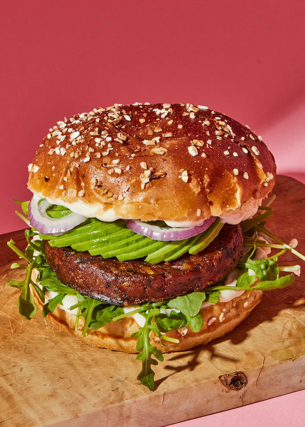 a hamburger with avocado onions and lettuce on a wooden cutting board