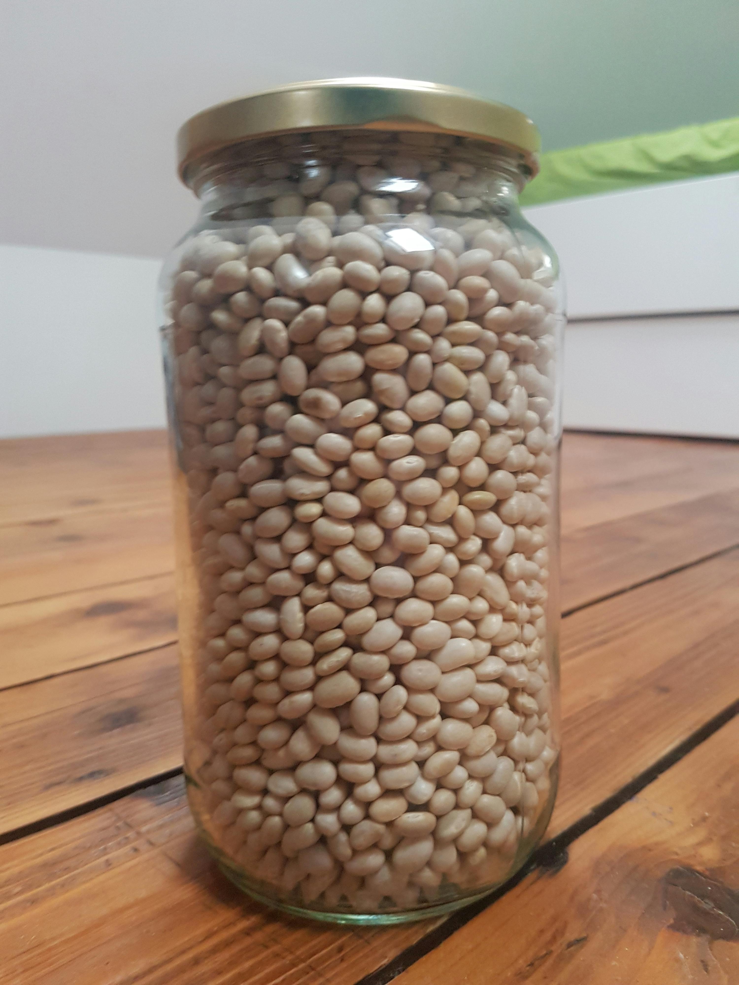 ein Glas gefüllt mit weißen Bohnen sitzt auf einem Holztisch