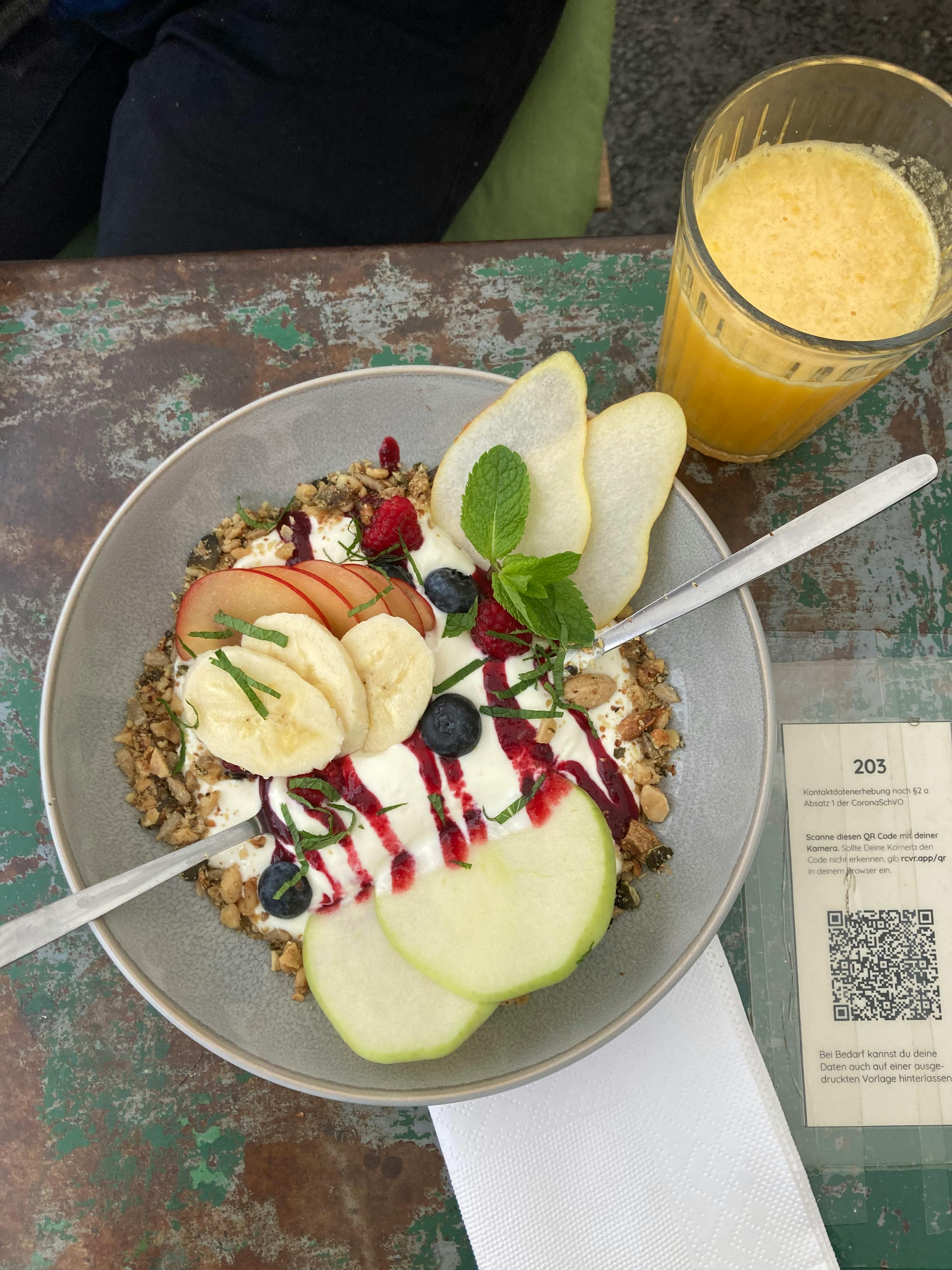 un bol de granola avec des fruits et du yogourt est assis sur une table à côté d' un verre de jus