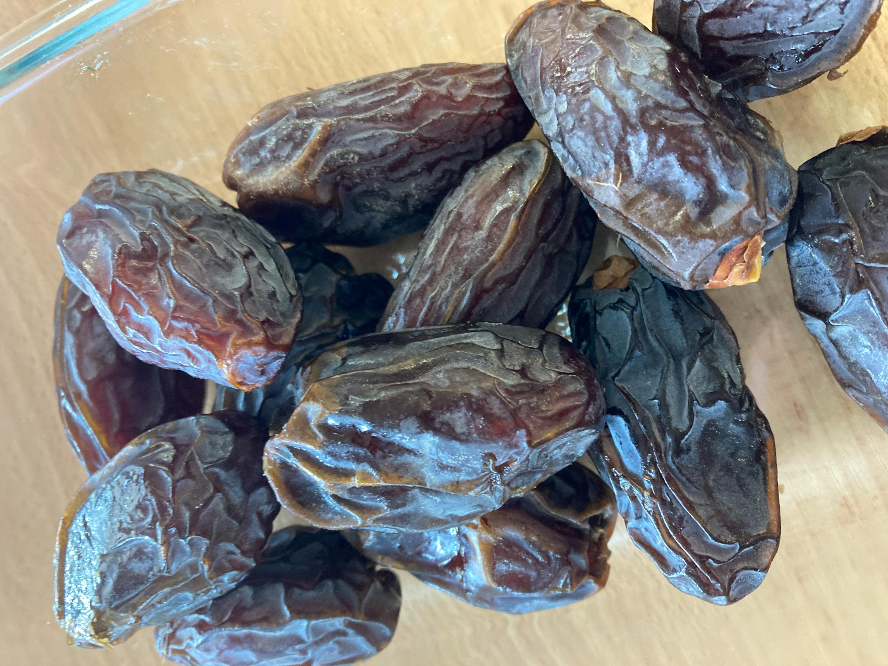 a glass container filled with dates on a wooden table