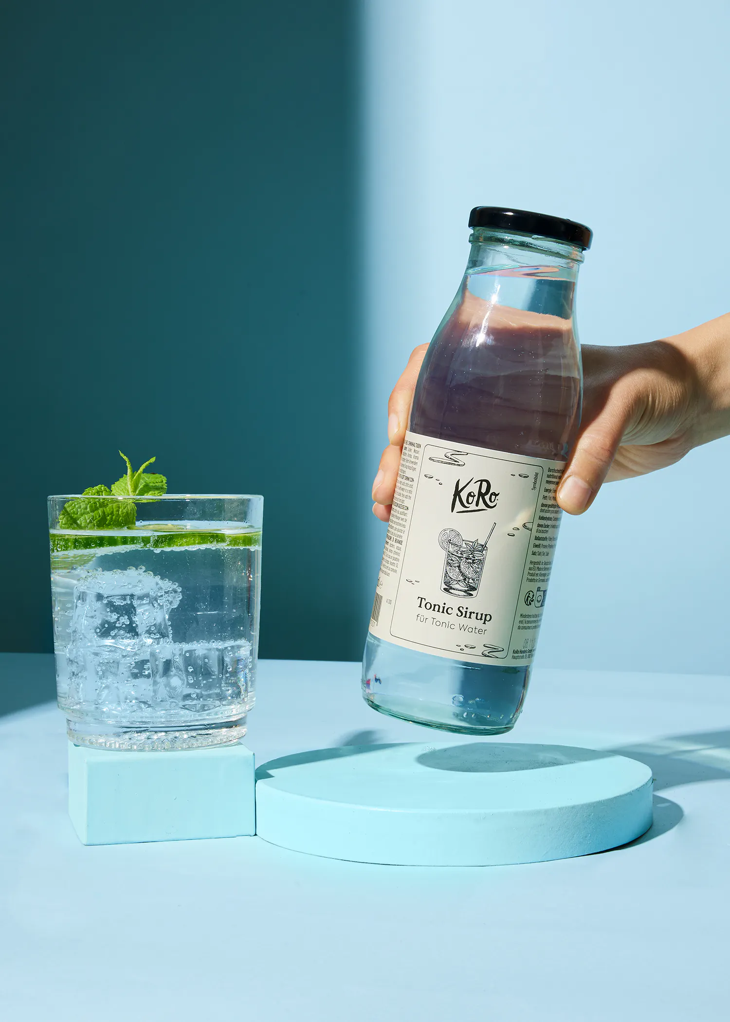 una persona sostiene una botella de sirope tonic sobre un vaso de agua