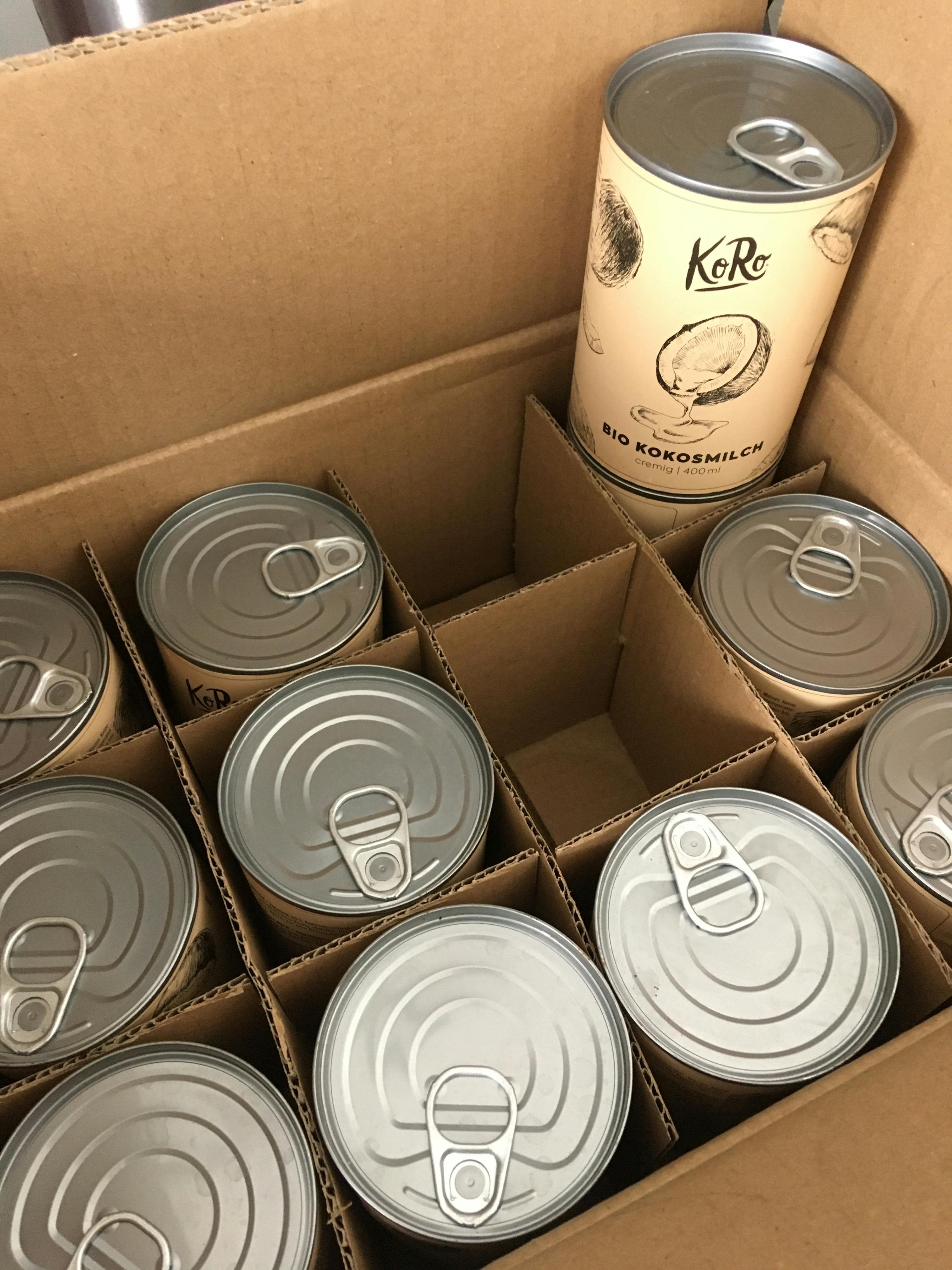 a cardboard box filled with several cans of keko