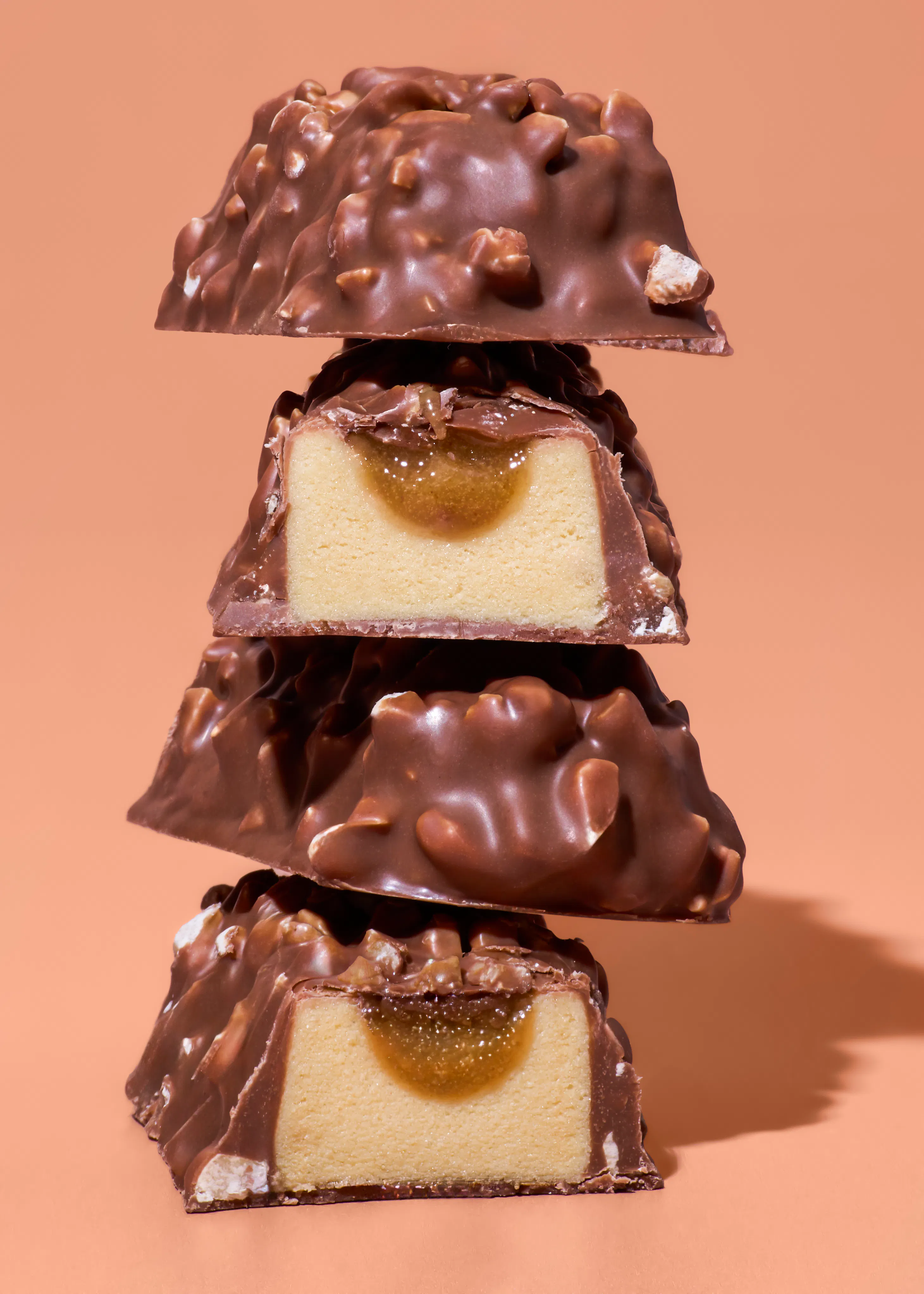 a stack of four chocolate-covered candies with nuts, two of which are cut open to reveal a light-colored filling with a gooey caramel center.